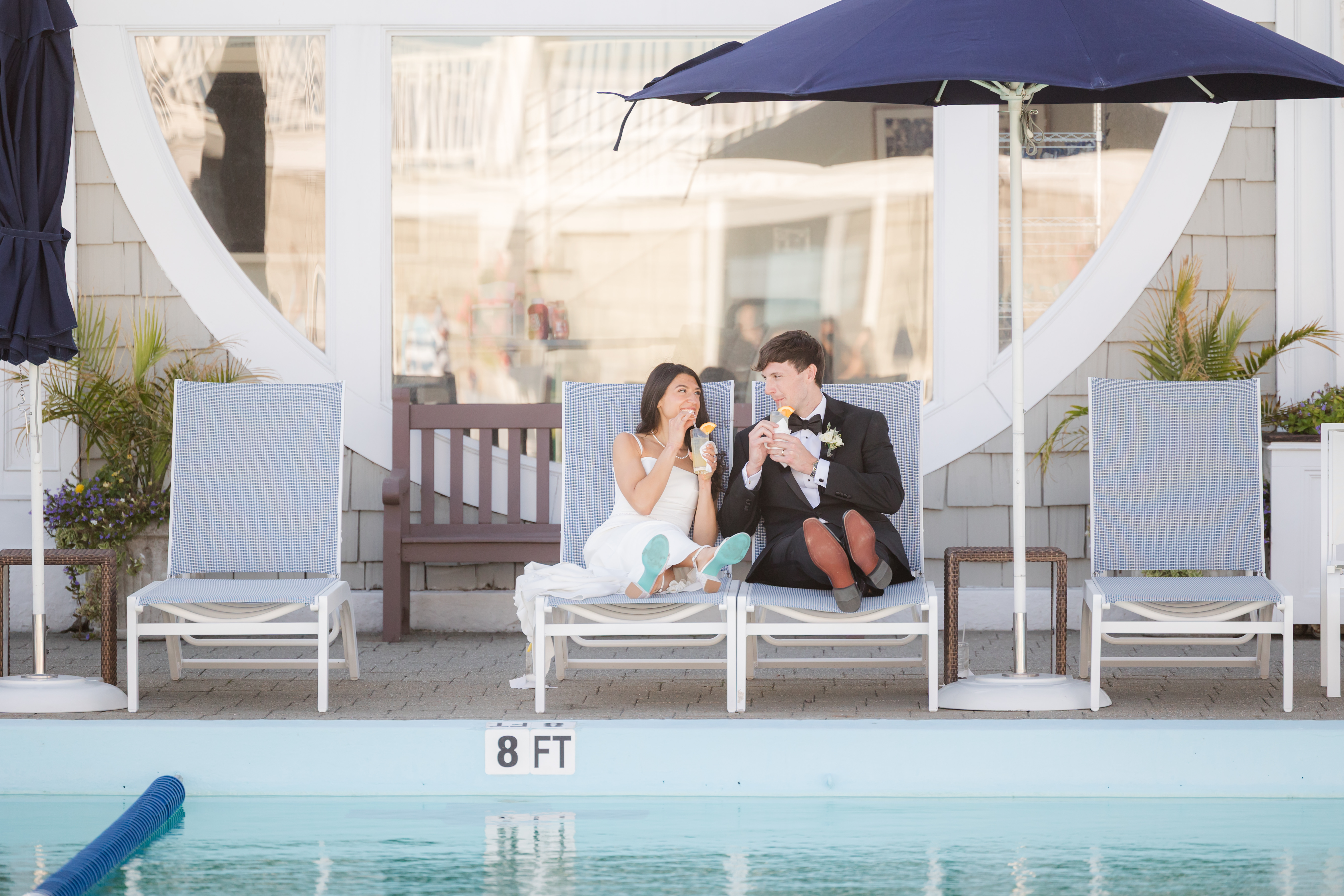 Bride and groom seated by the poolside, looking and smiling at each other