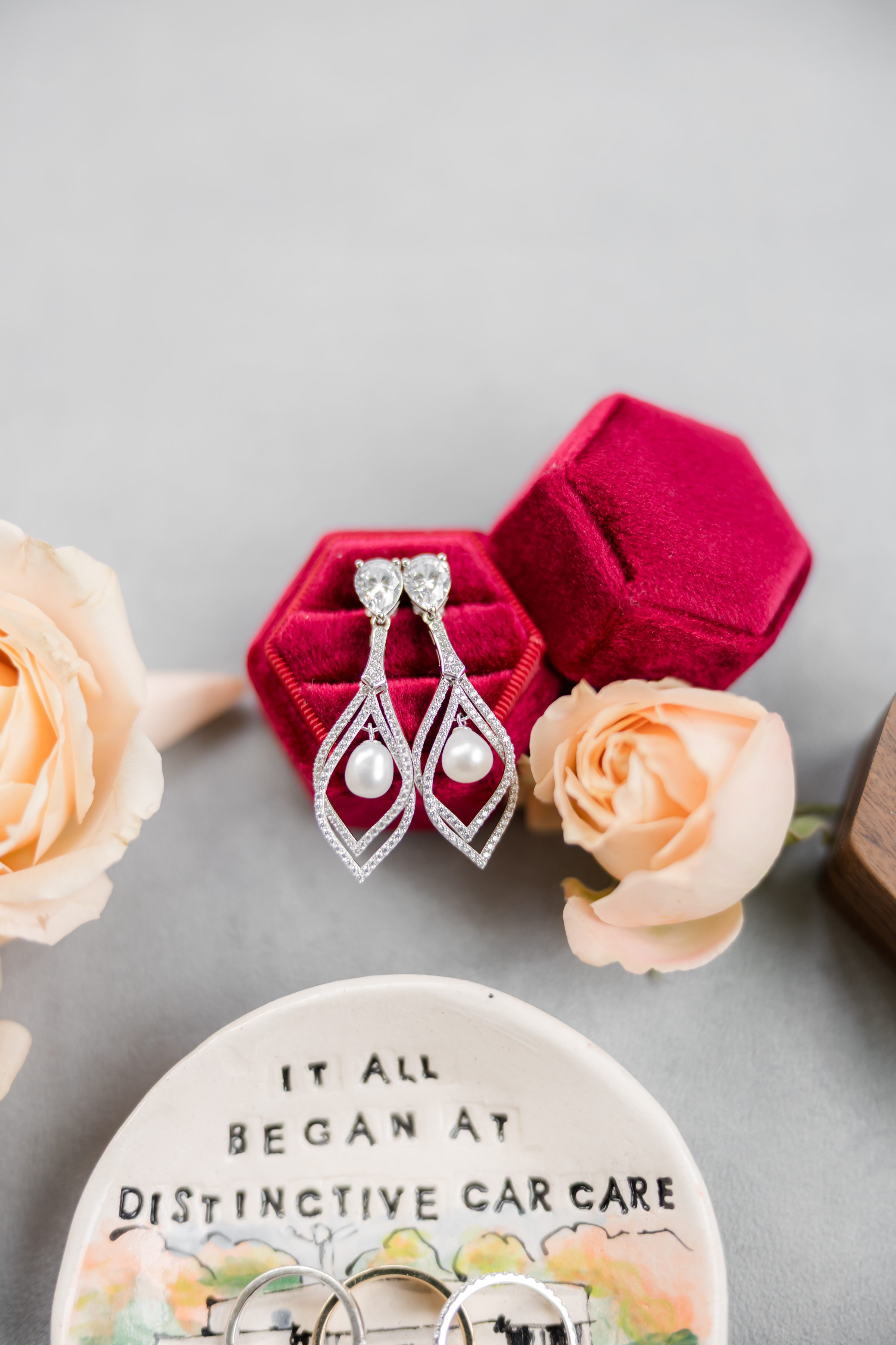 Elegant bridal earrings displayed in a red velvet box with roses nearby and wedding rings