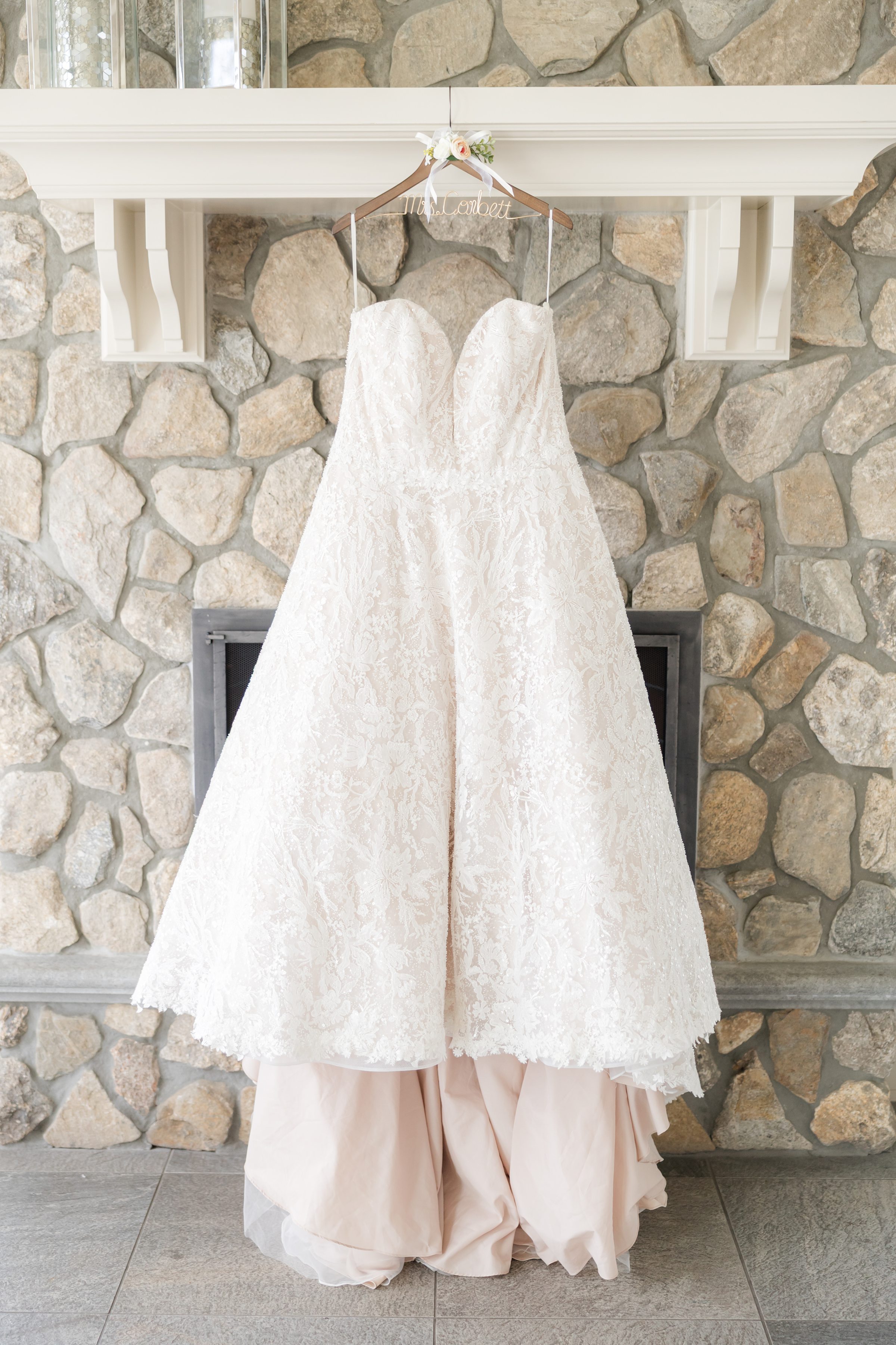 Wedding dress hanging in front of a stone fireplace on a custom hanger
