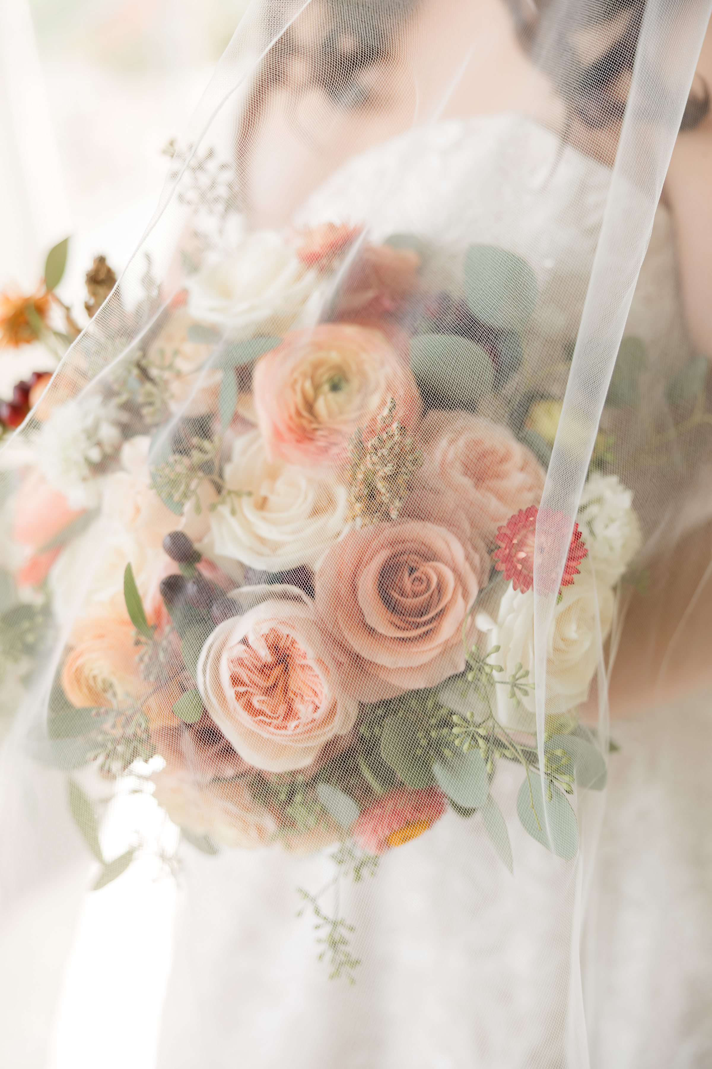 Bridal bouquet with peach, blush, and white flowers seen through a sheer veil