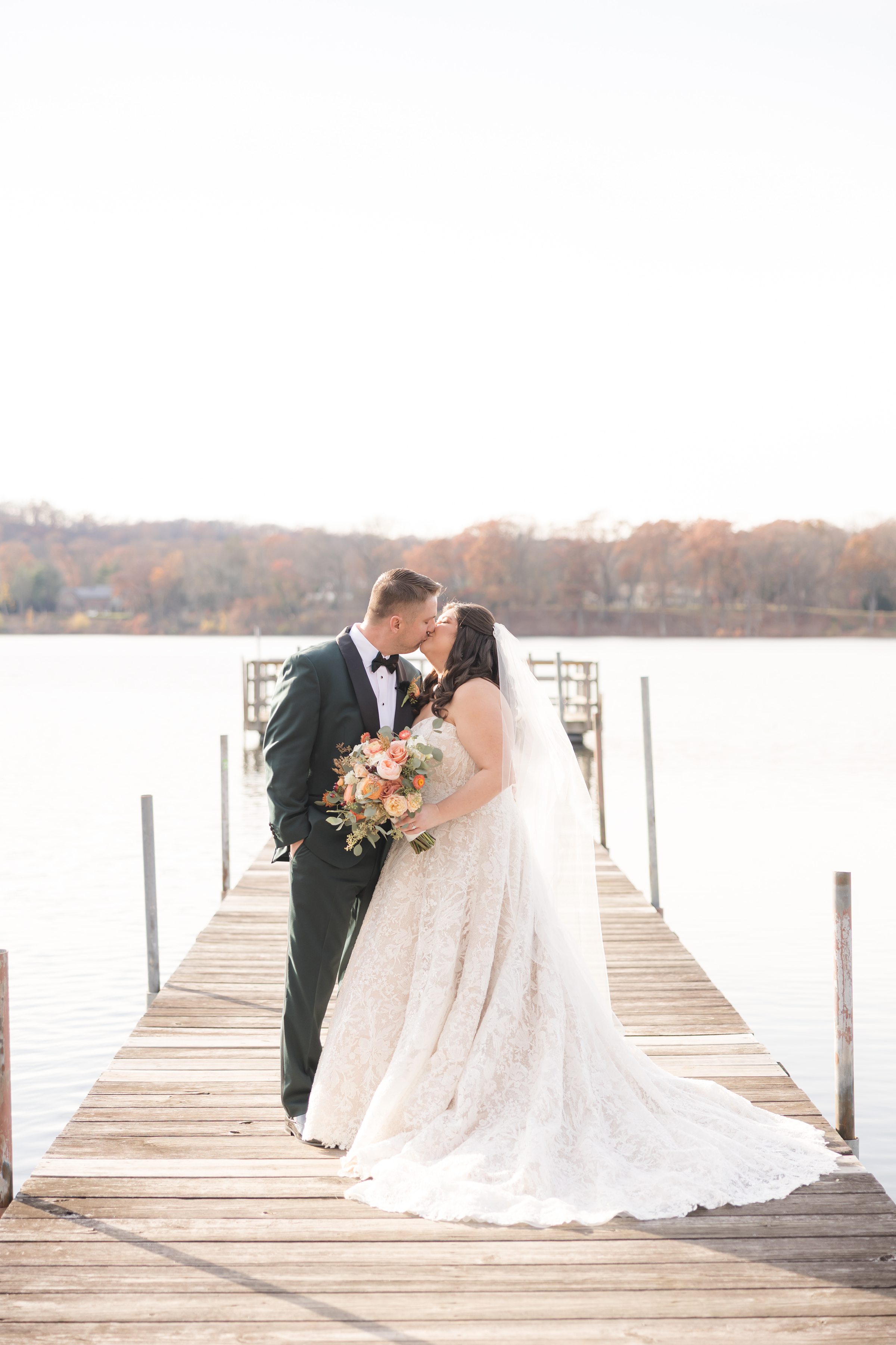 Bride and groom kissing on a dock with lake and soft autumn background