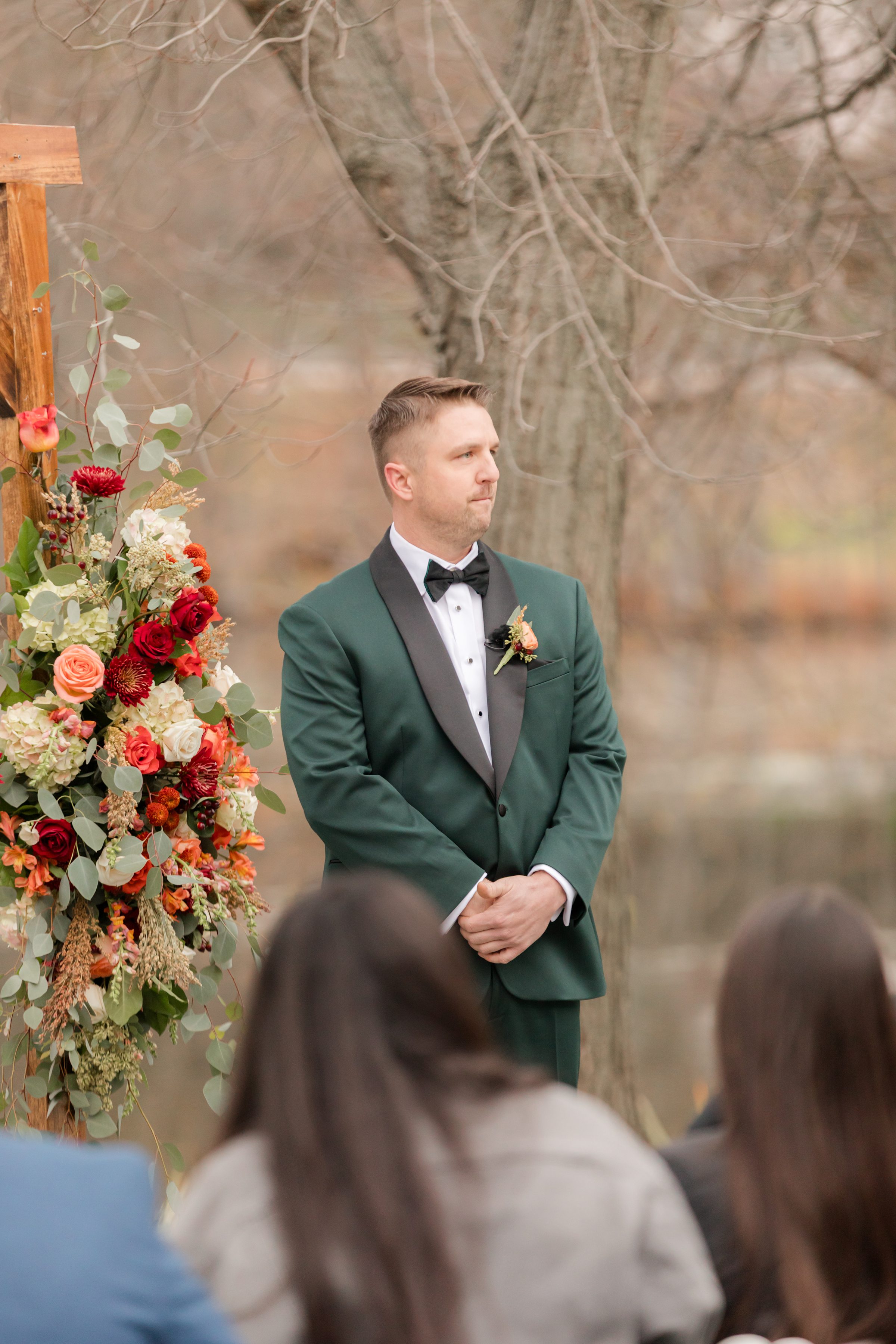 Groom standing at the altar beside a floral arrangement, looking ahead as he waits during the ceremony