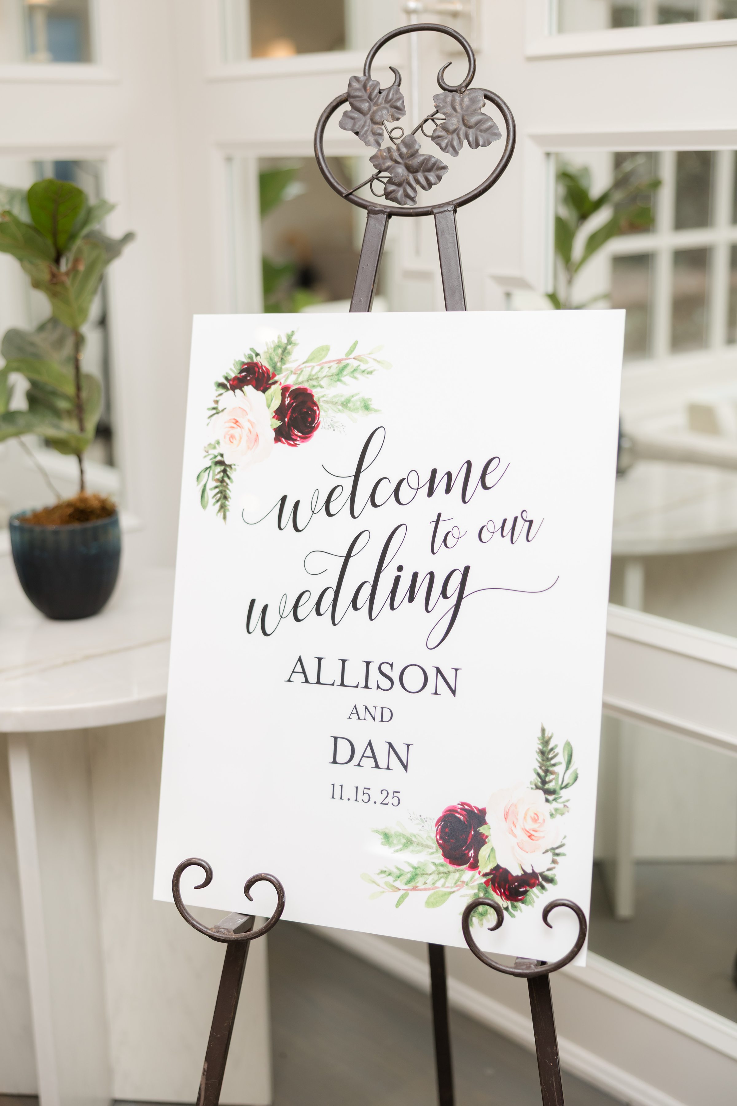 Welcome sign on an easel reading “Welcome to our wedding, Allison and Dan, 11.15.25,” decorated with floral accents