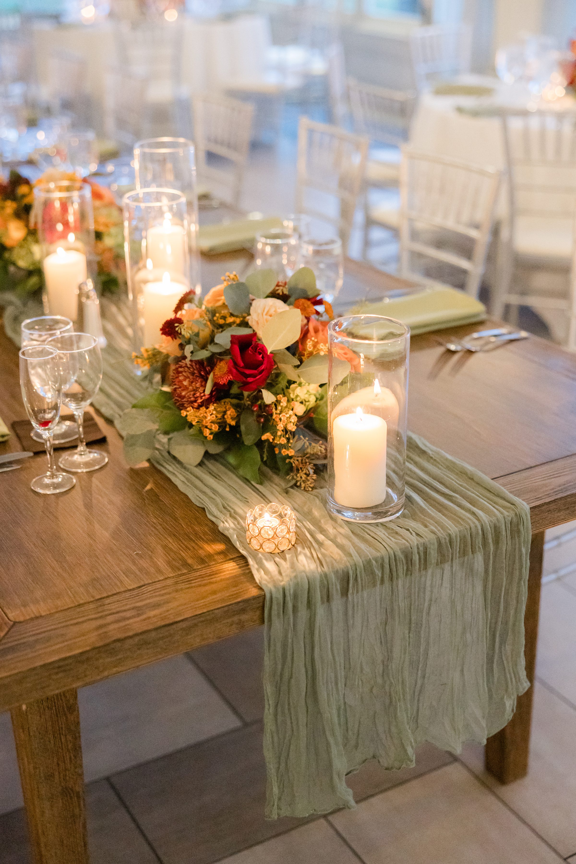 Elegant table centerpiece with candles and a floral arrangement on a wooden reception table