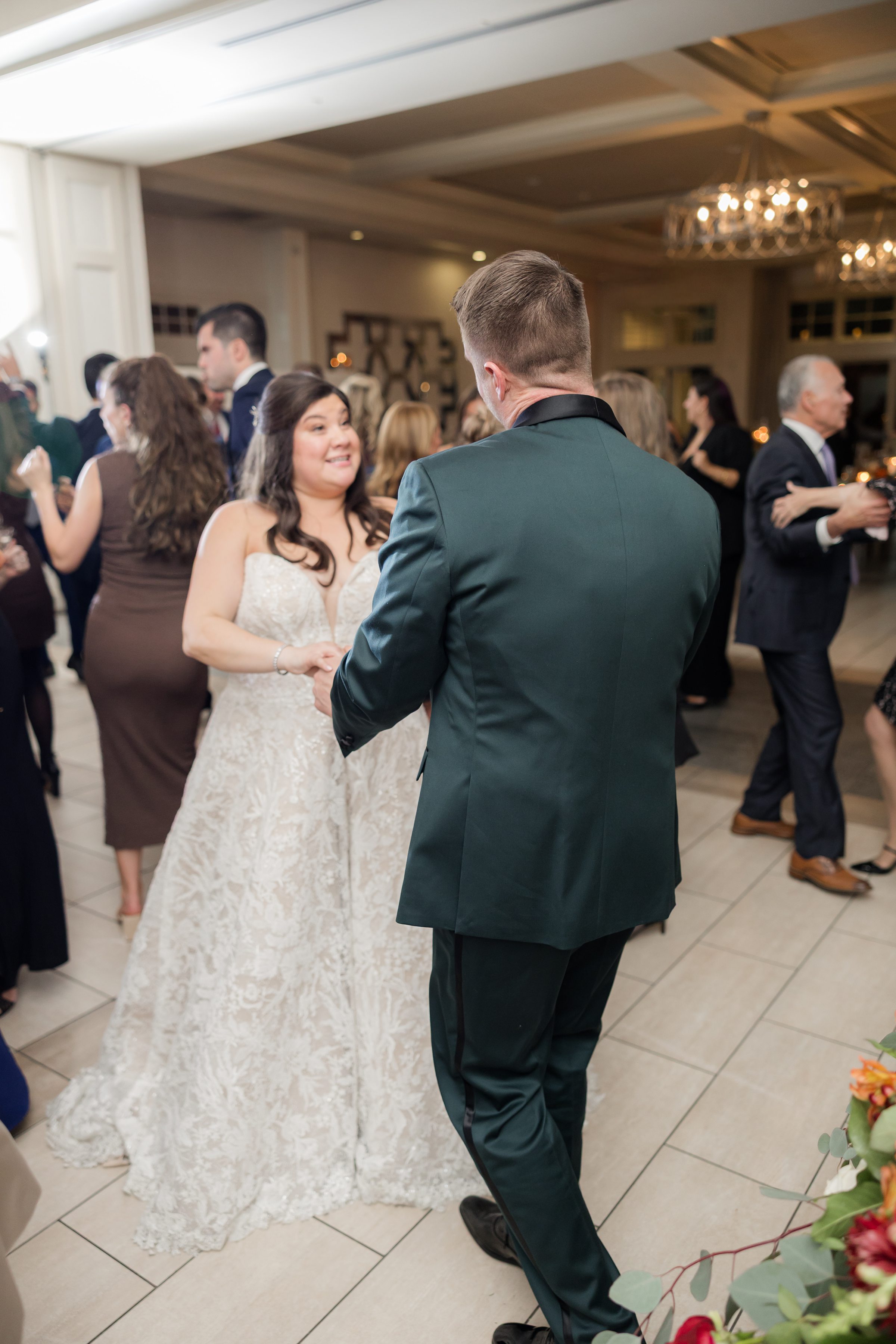 Bride and groom dance together, seen from behind, surrounded by guests.