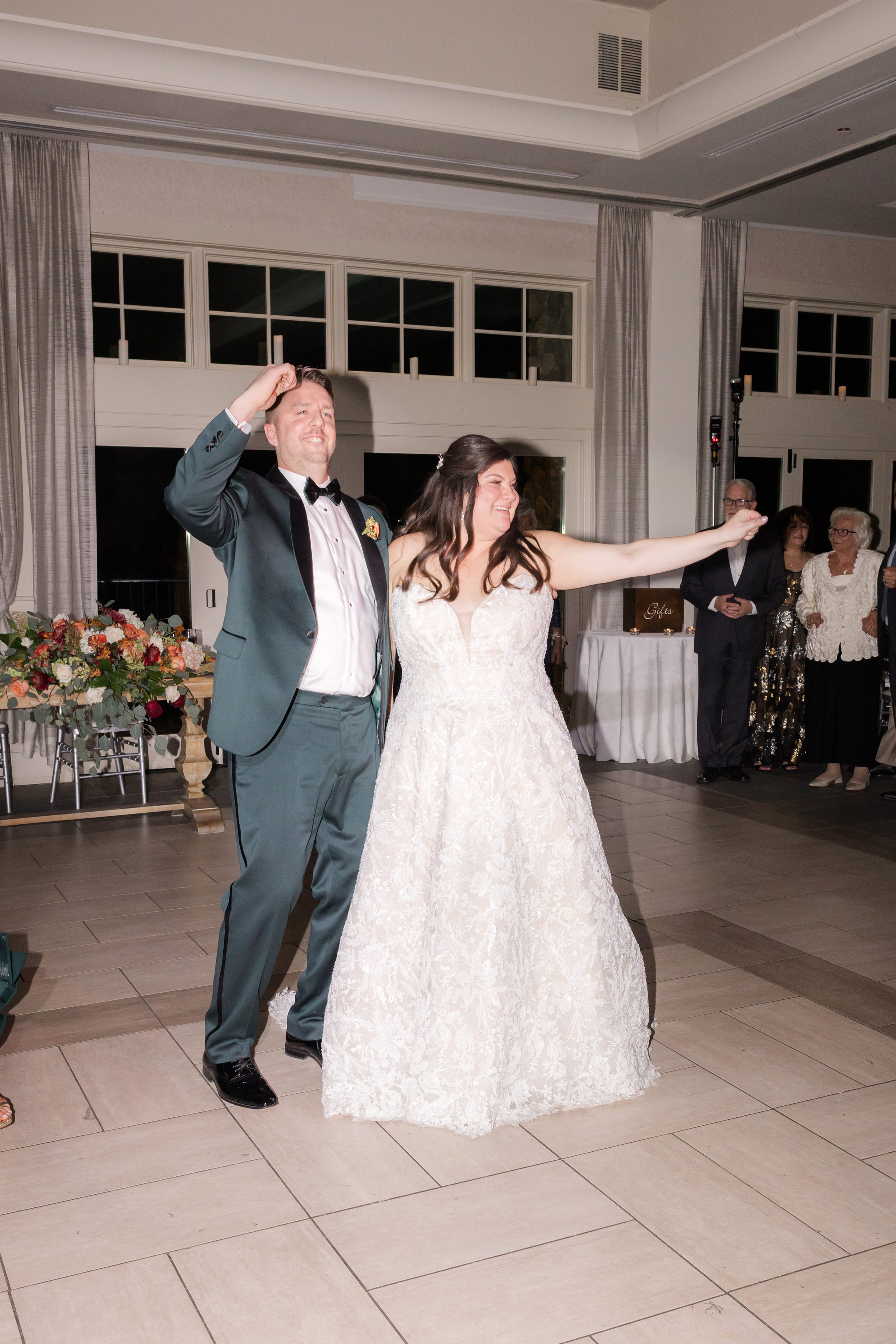 Bride and groom make a joyful entrance into the reception, holding hands and smiling as they step onto the dance floor while guests look on