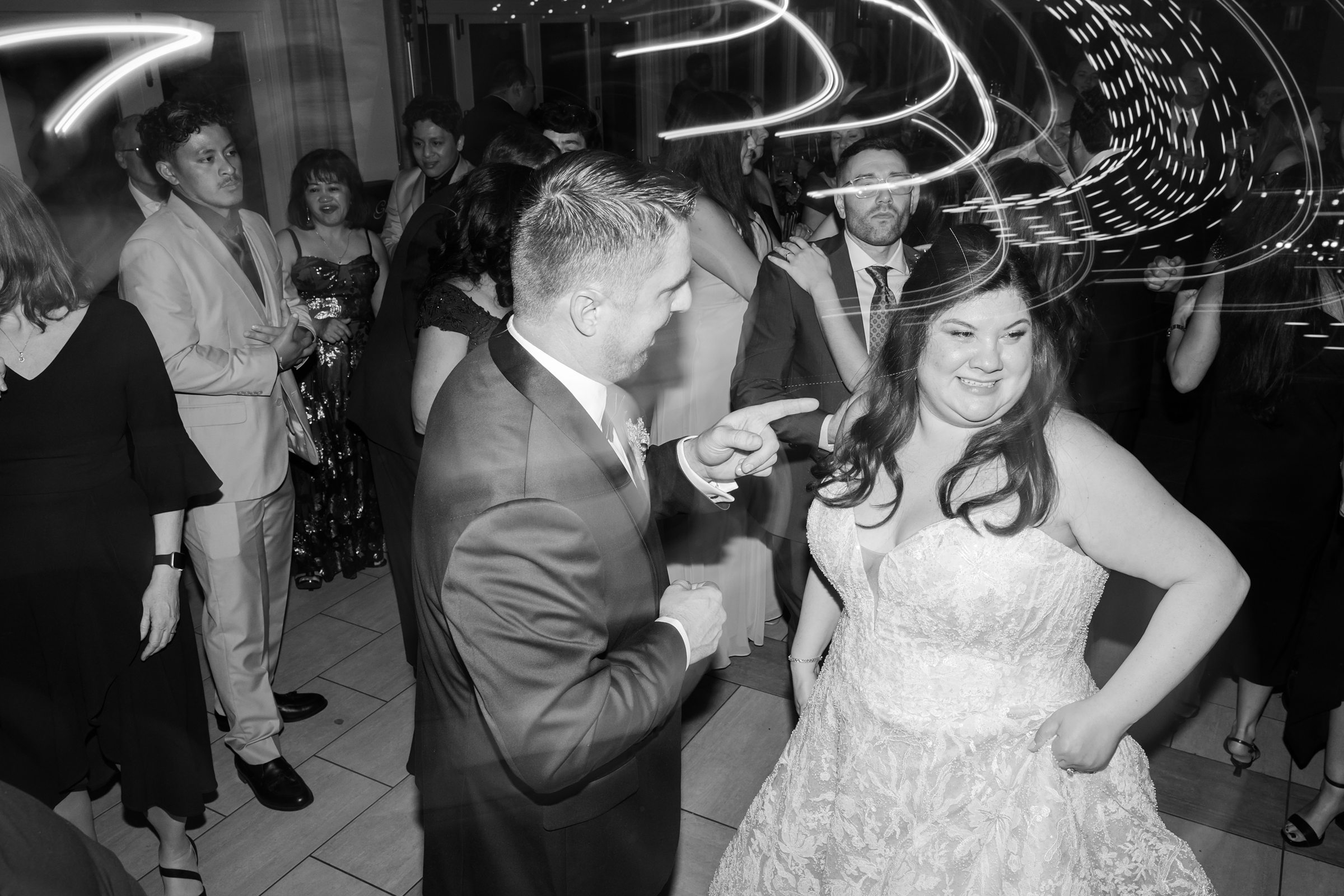 Bride and groom dance in a crowded reception, with motion-blur light trails swirling above them
