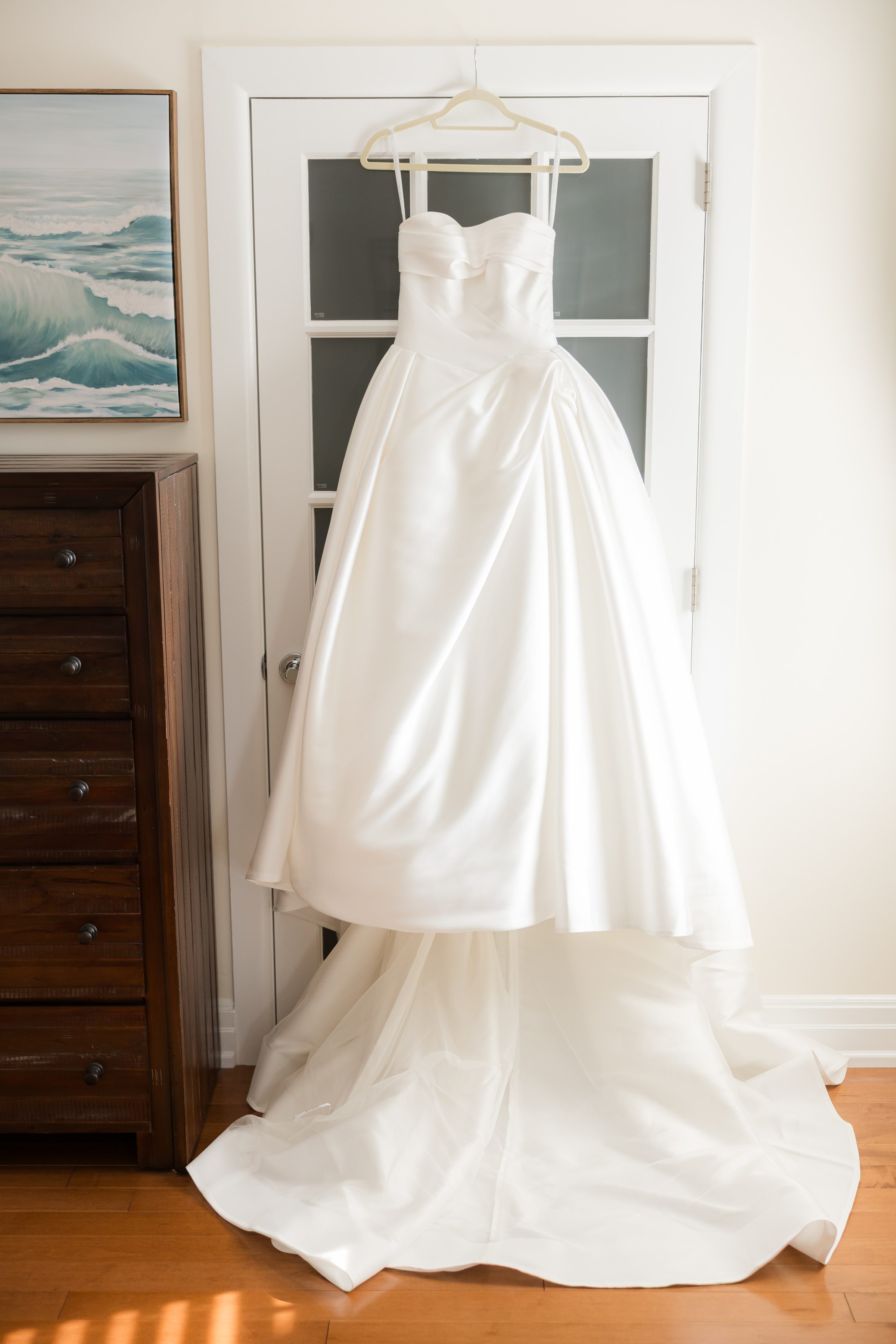 White wedding dress hanging on a door with a long train spread on the floor.