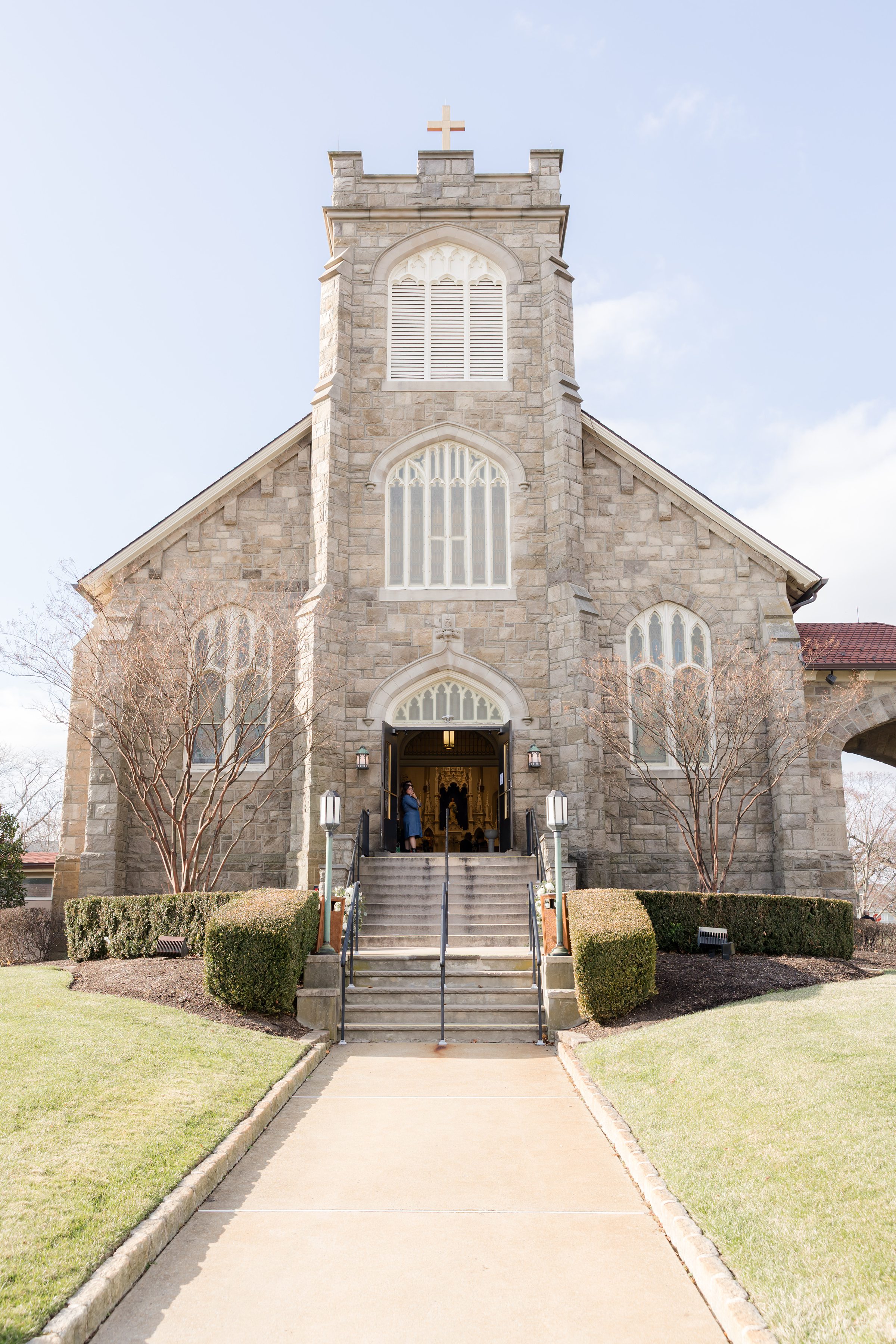 Stone church with a tall central tower and cross at the top, featuring arched windows and steps leading to the open front entrance.