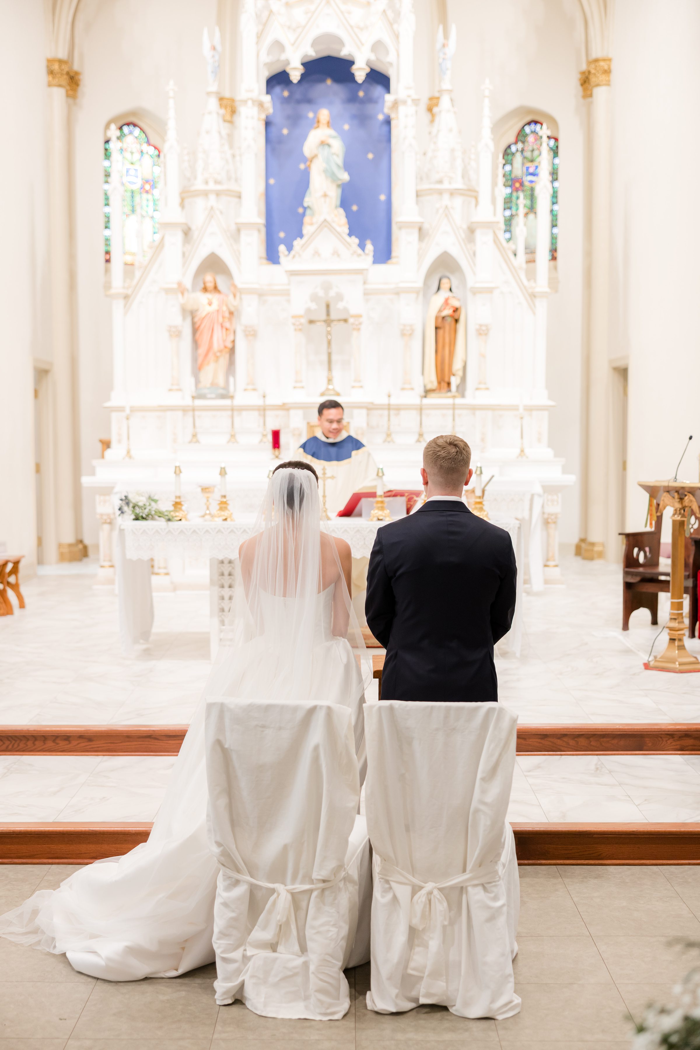 Bride and groom standing together at the altar during their wedding ceremony, facing the officiant inside an ornate church.