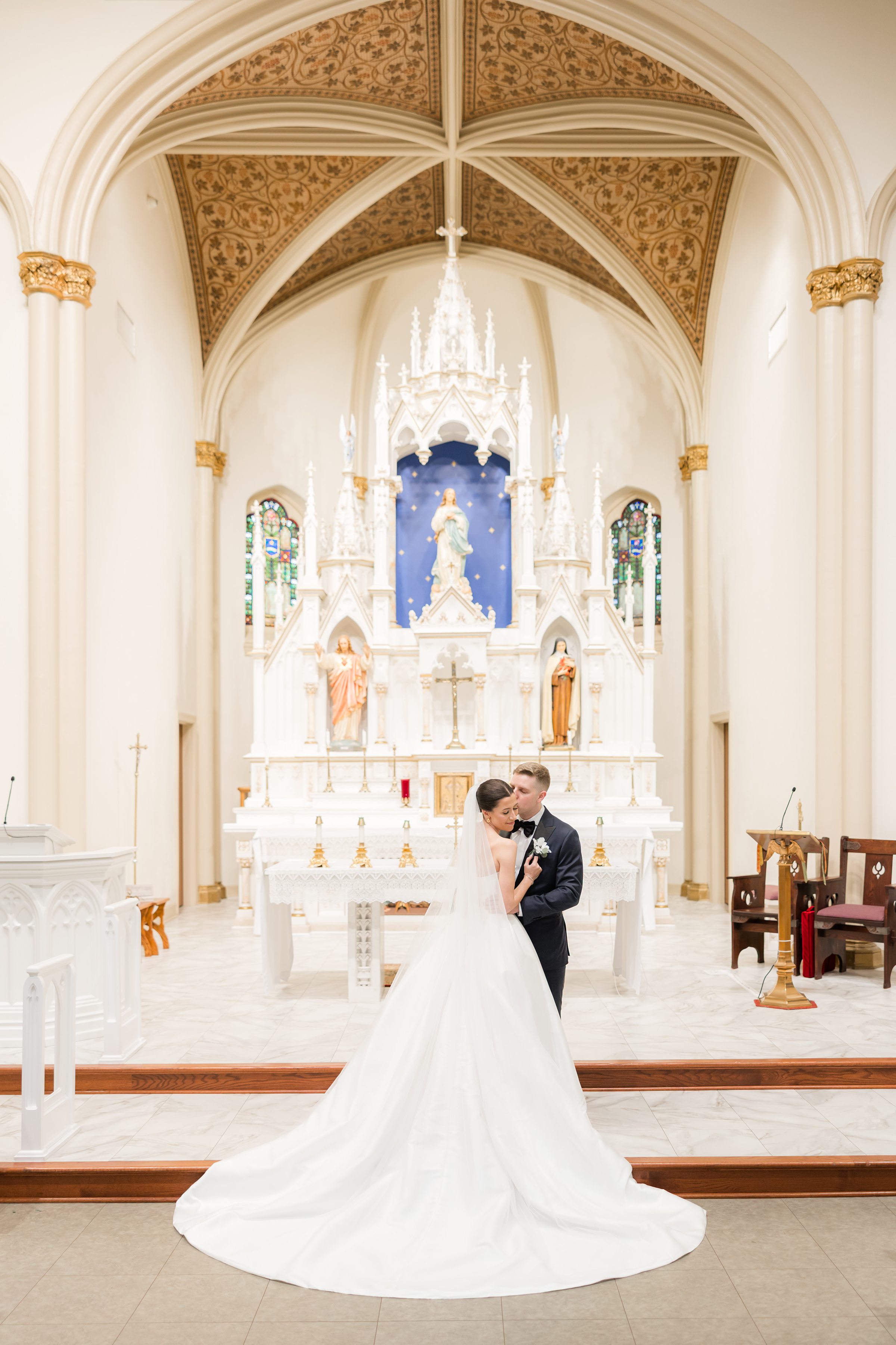 Bride and groom embracing inside a church in front of an ornate altar.