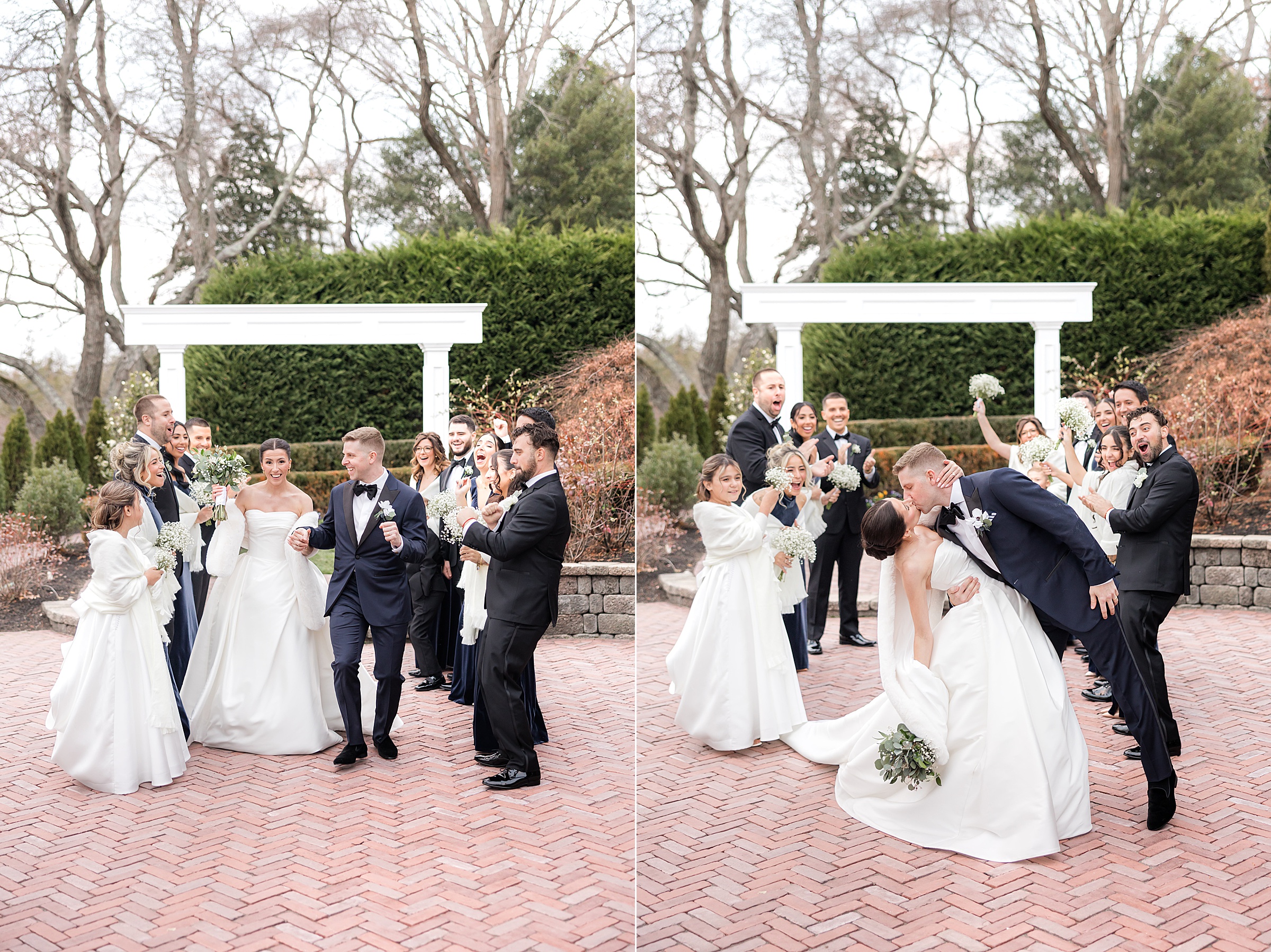 Bride and groom share a romantic dip kiss while their wedding party cheers around them under a garden arbor.