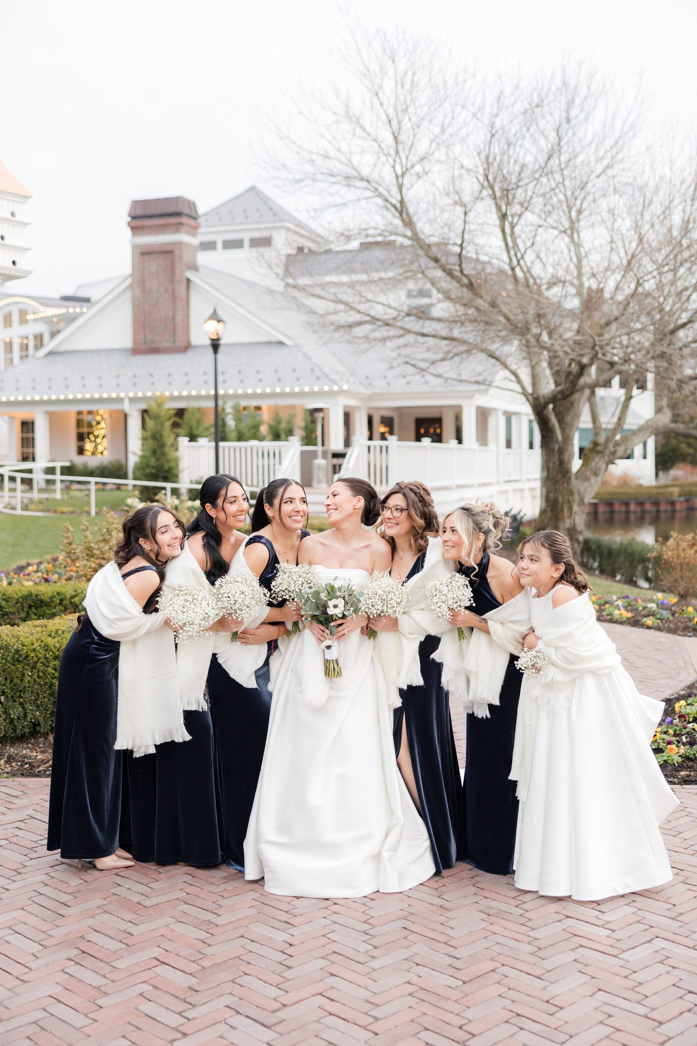 Bride surrounded by bridesmaids and flower girls in coordinated dresses, smiling together.