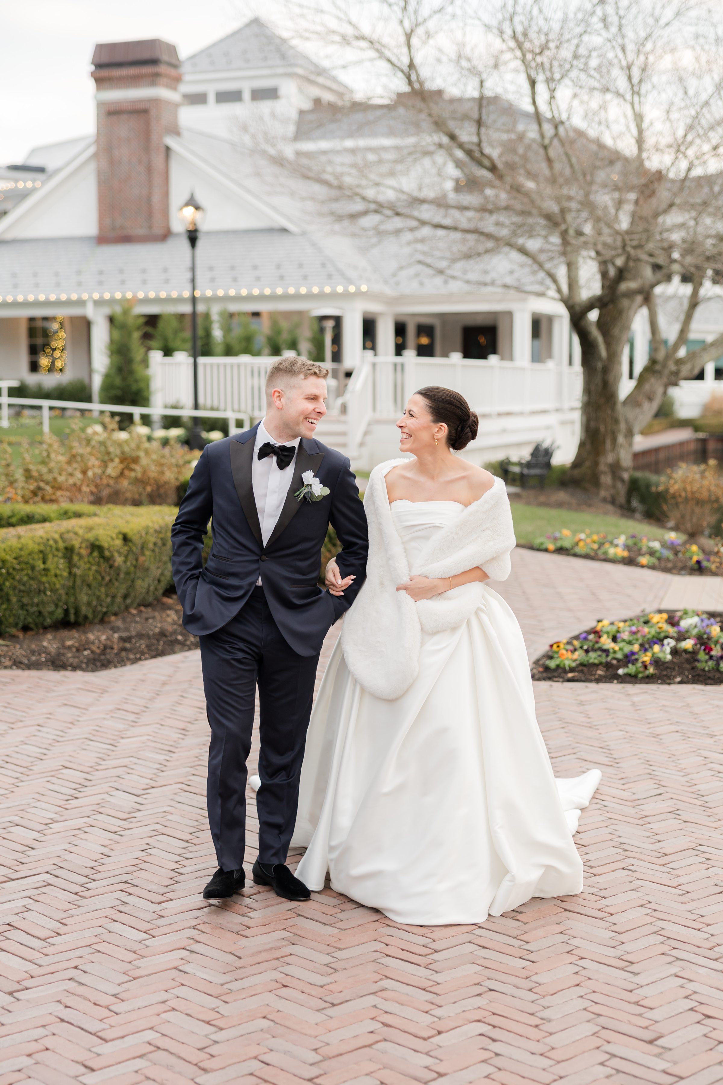 Bride and groom walking together on a brick courtyard, smiling at each other.