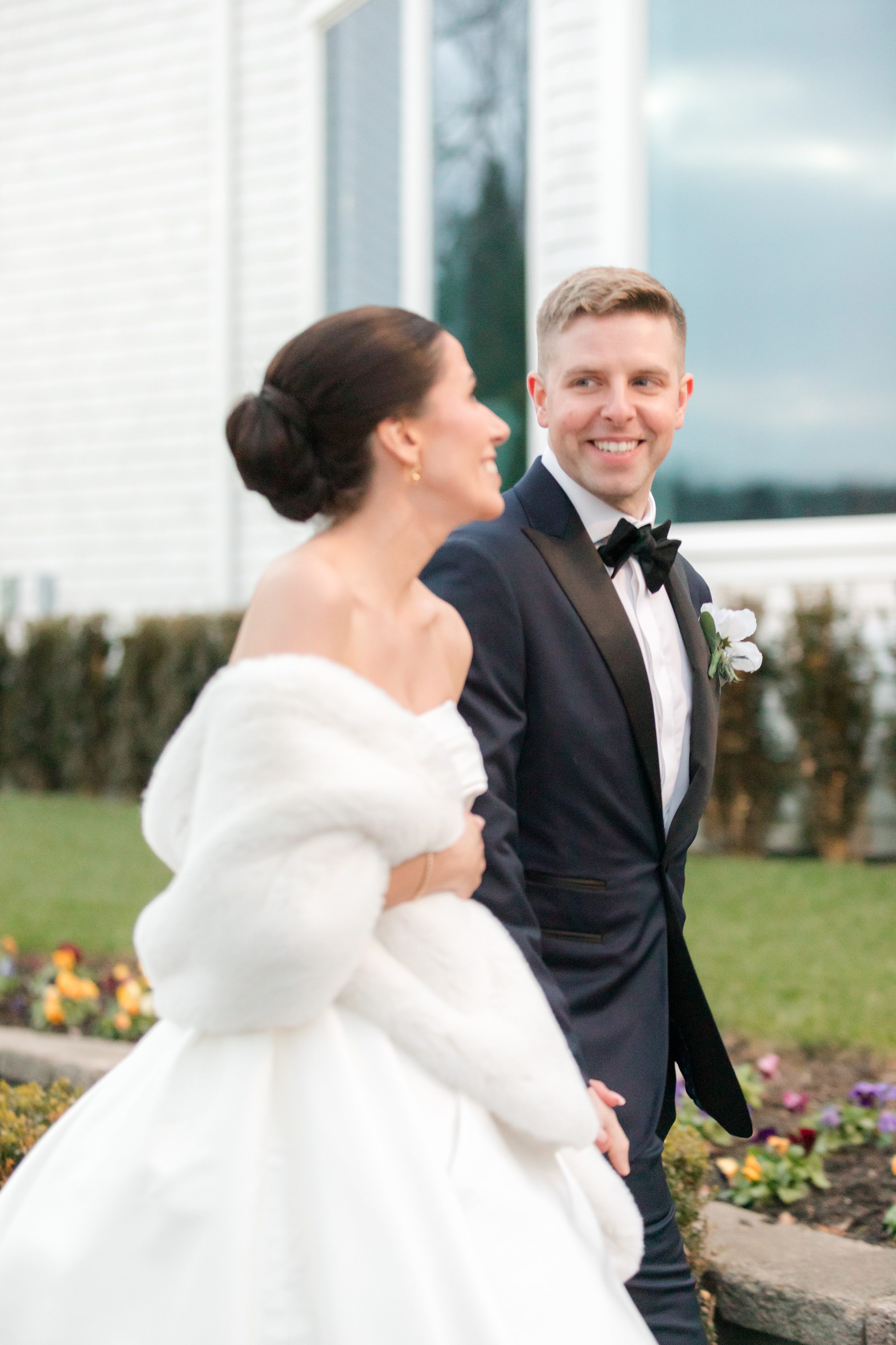 Groom looking at bride with a smile while walking beside her in a garden setting.