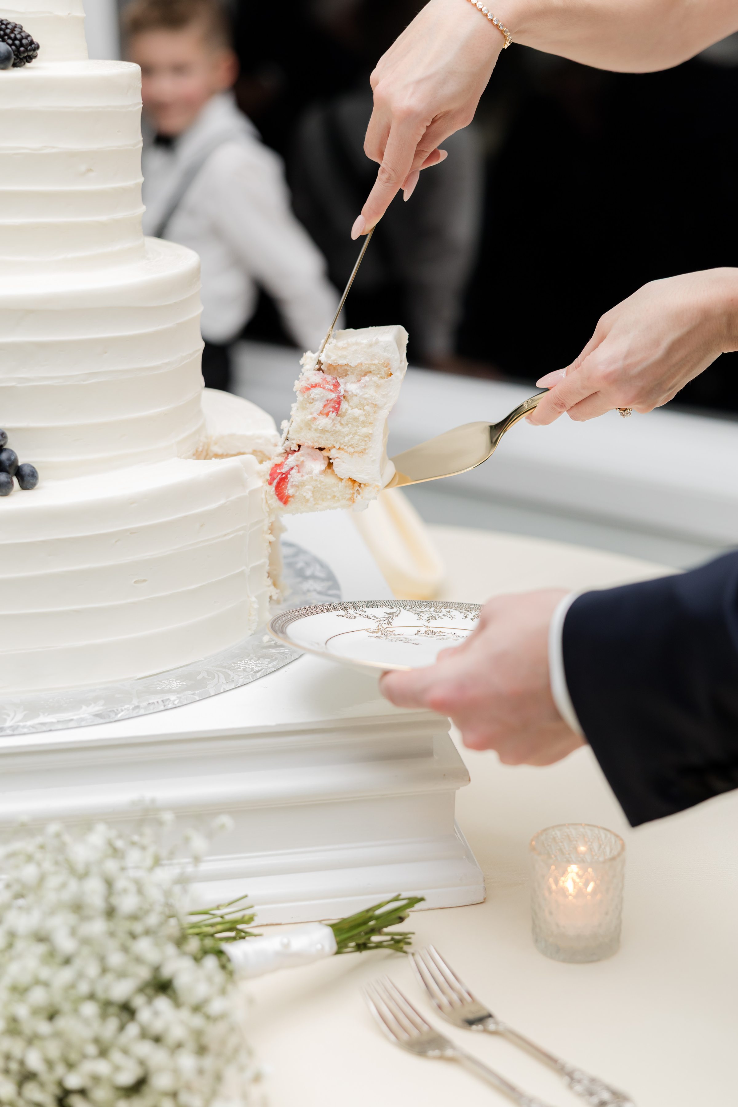 Bride and groom cutting and serving a slice of white wedding cake with strawberry filling onto a plate.