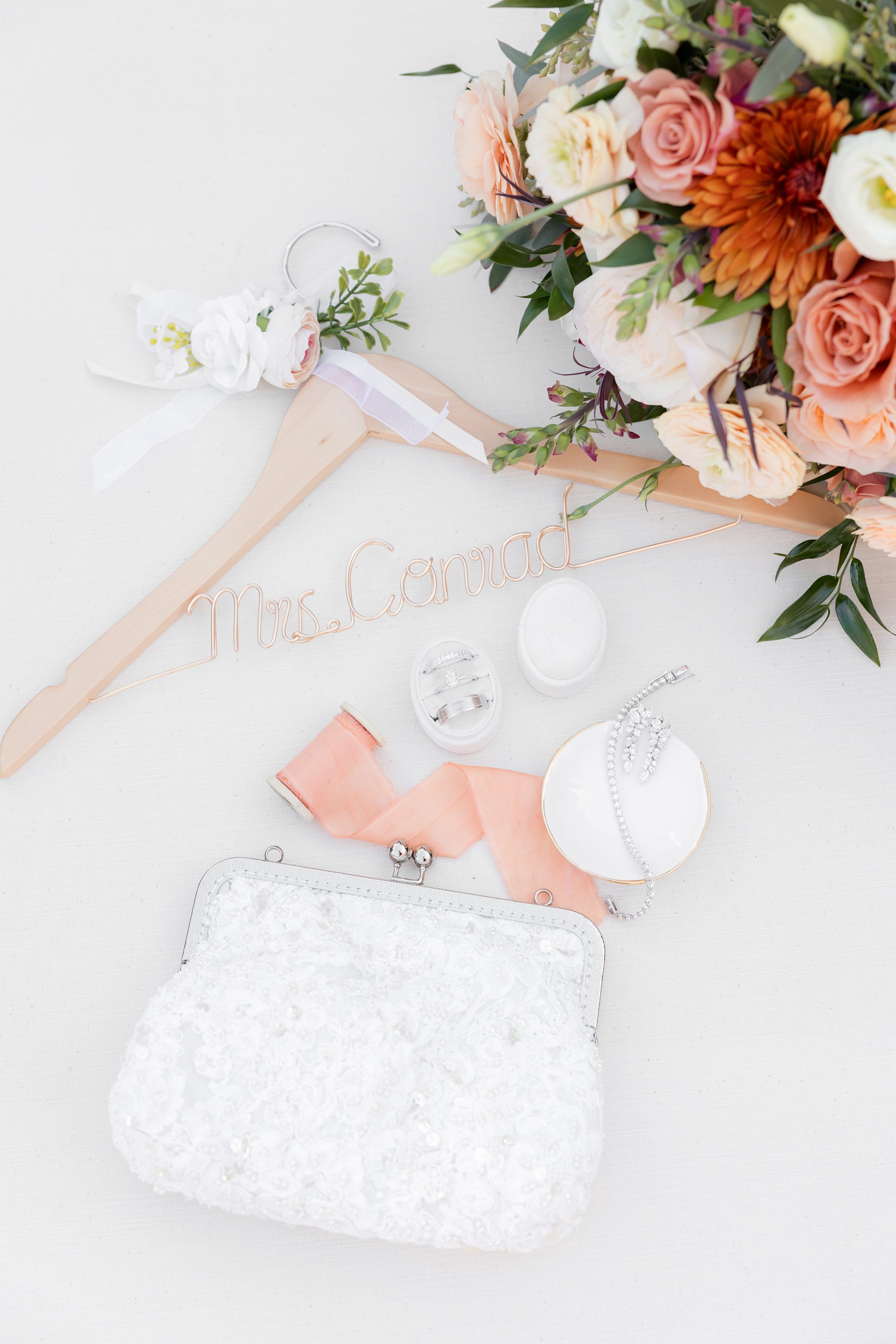 Personalized hanger, bouquet, jewelry, ring box, ribbon, and beaded clutch on a white background.