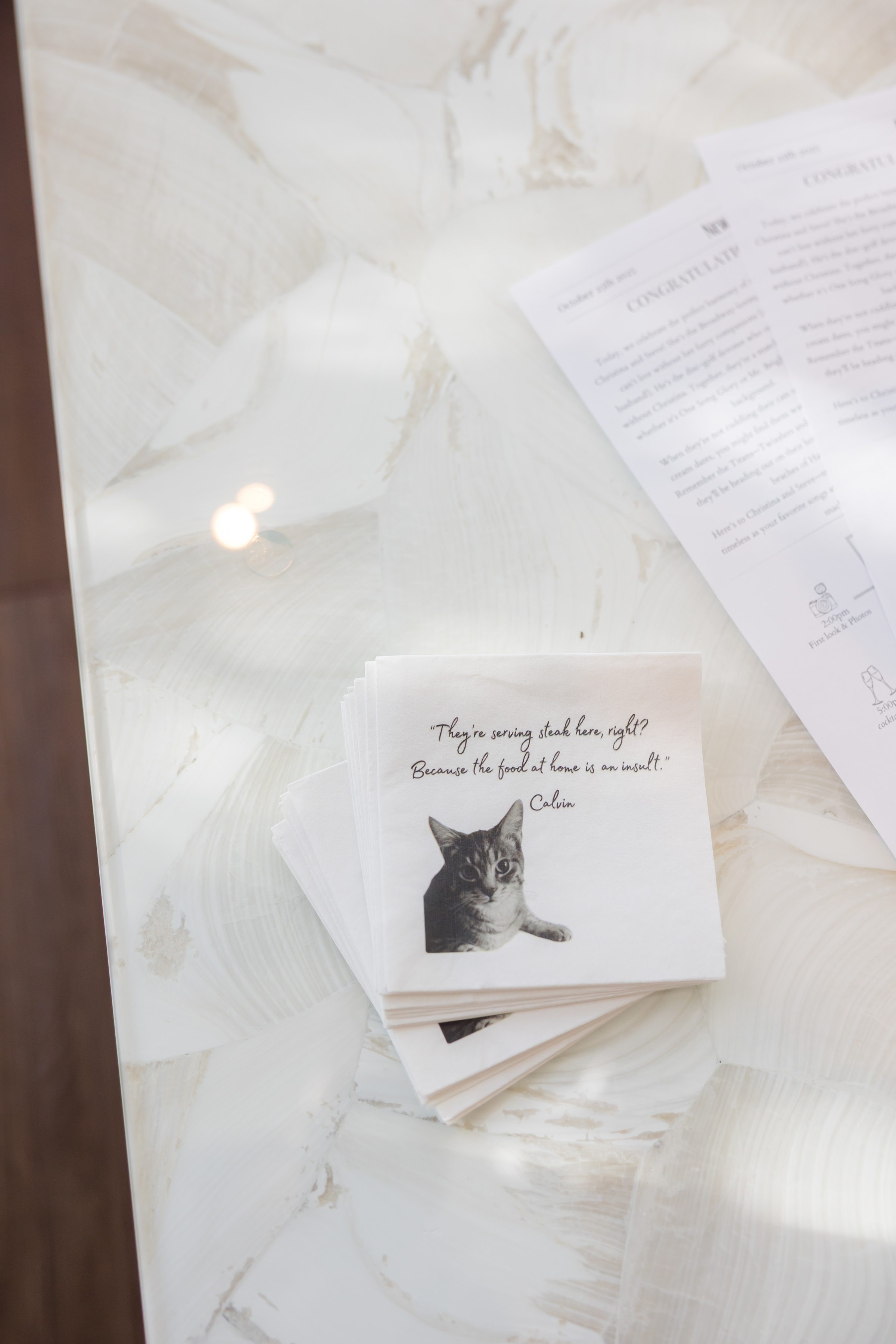 Wedding program and napkin with a cat illustration and humorous quote displayed on a table.