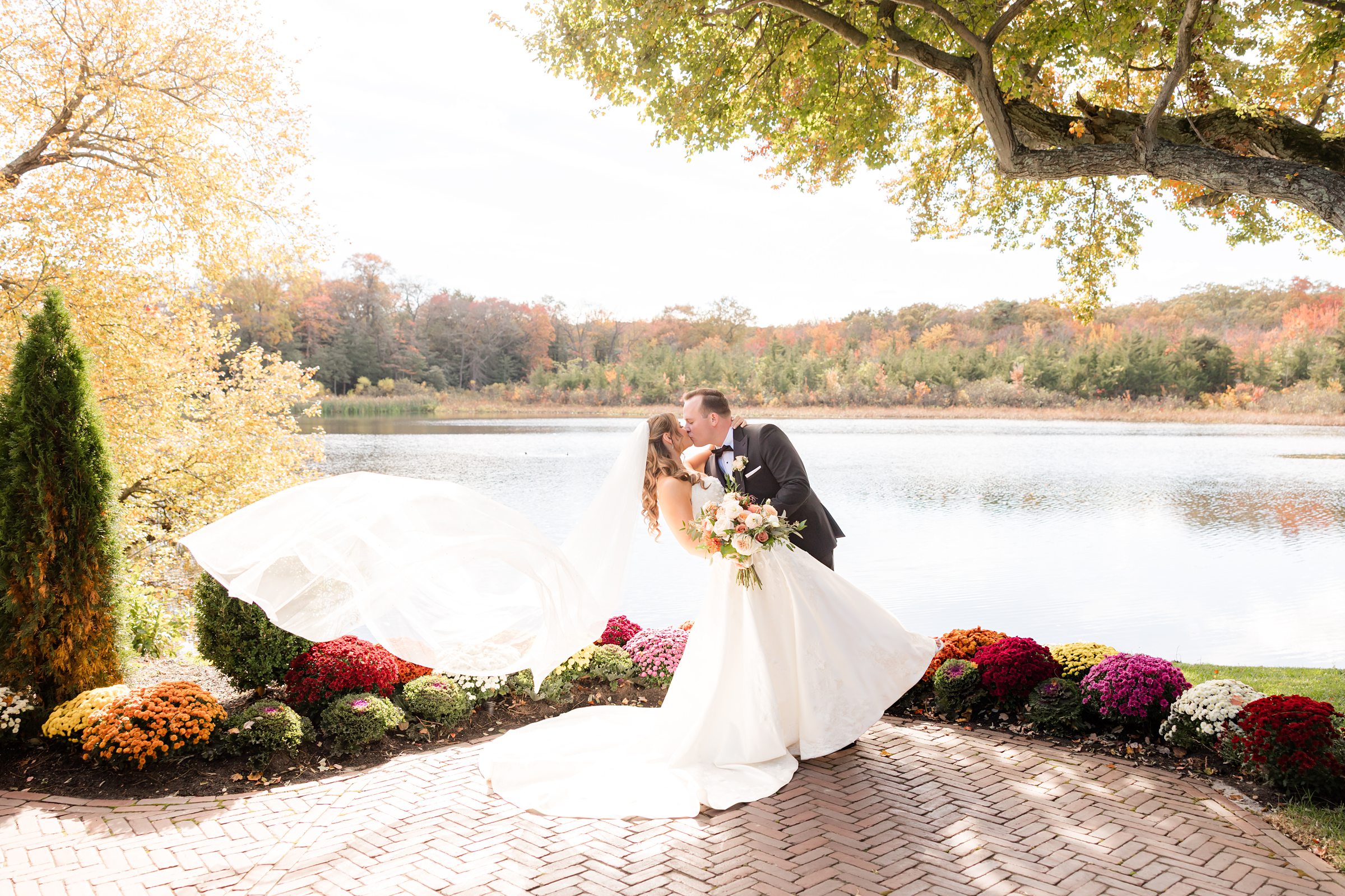 Dramatic dip kiss by the lake as the bride’s veil flows in the air behind them.