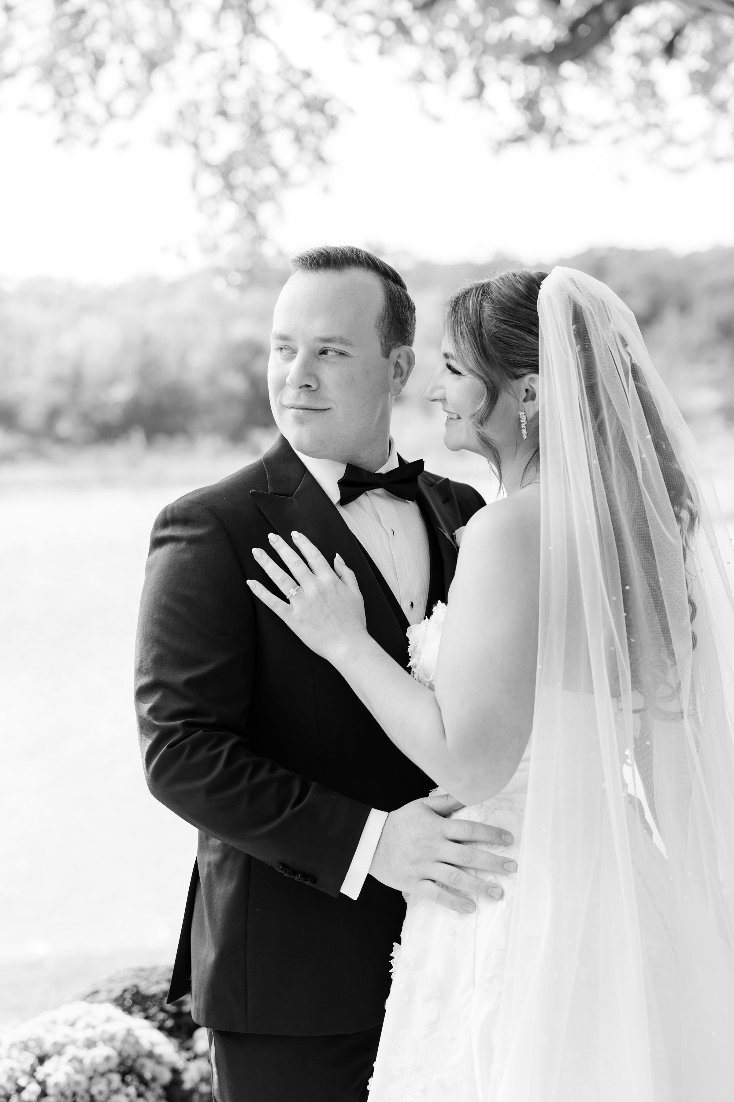 Bride and groom embracing, the bride resting her hand on his chest as they share a quiet, intimate moment outdoors.