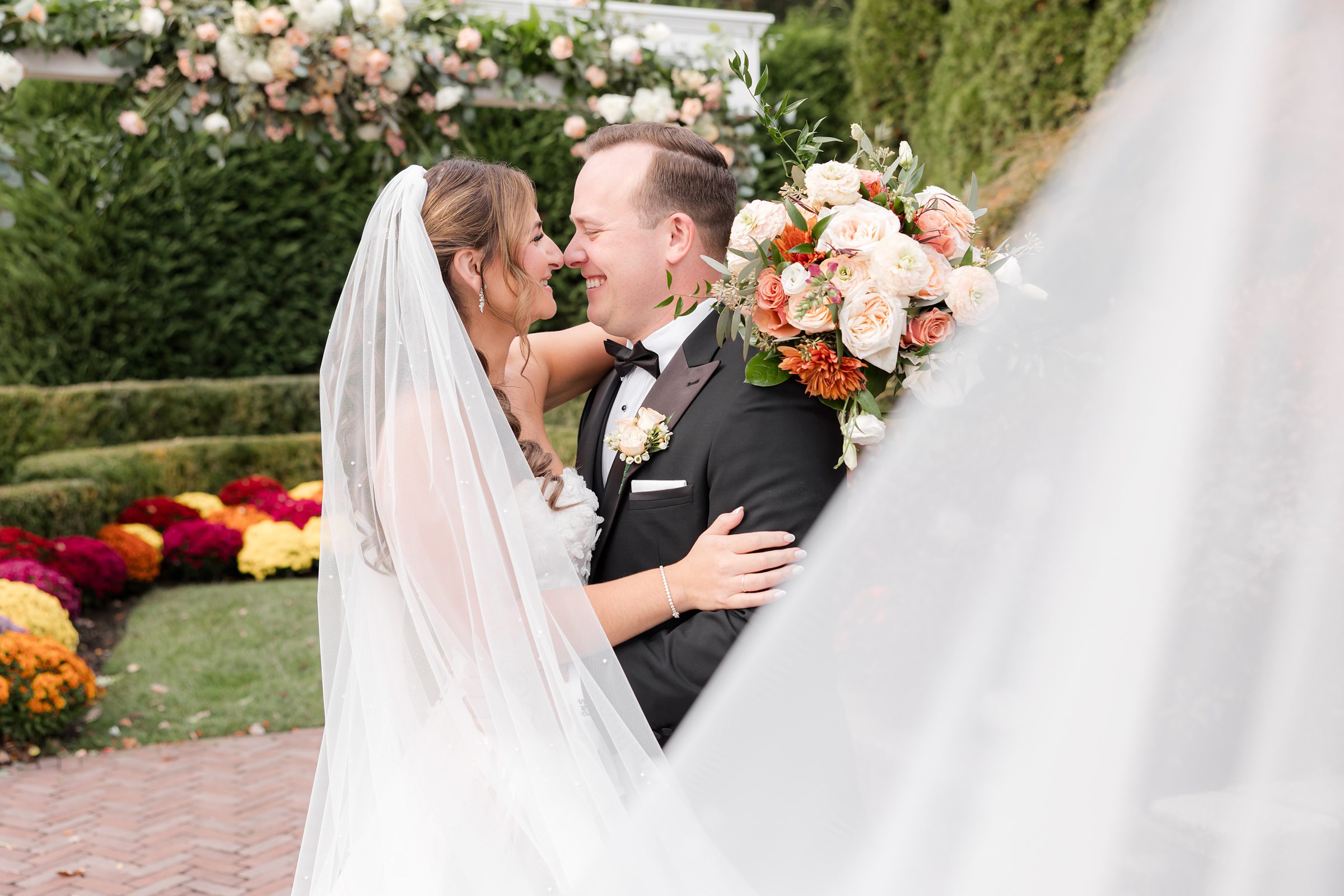 Bride and groom share a tender, intimate moment, smiling softly at each other as her veil gently frames them in a romantic garden setting.