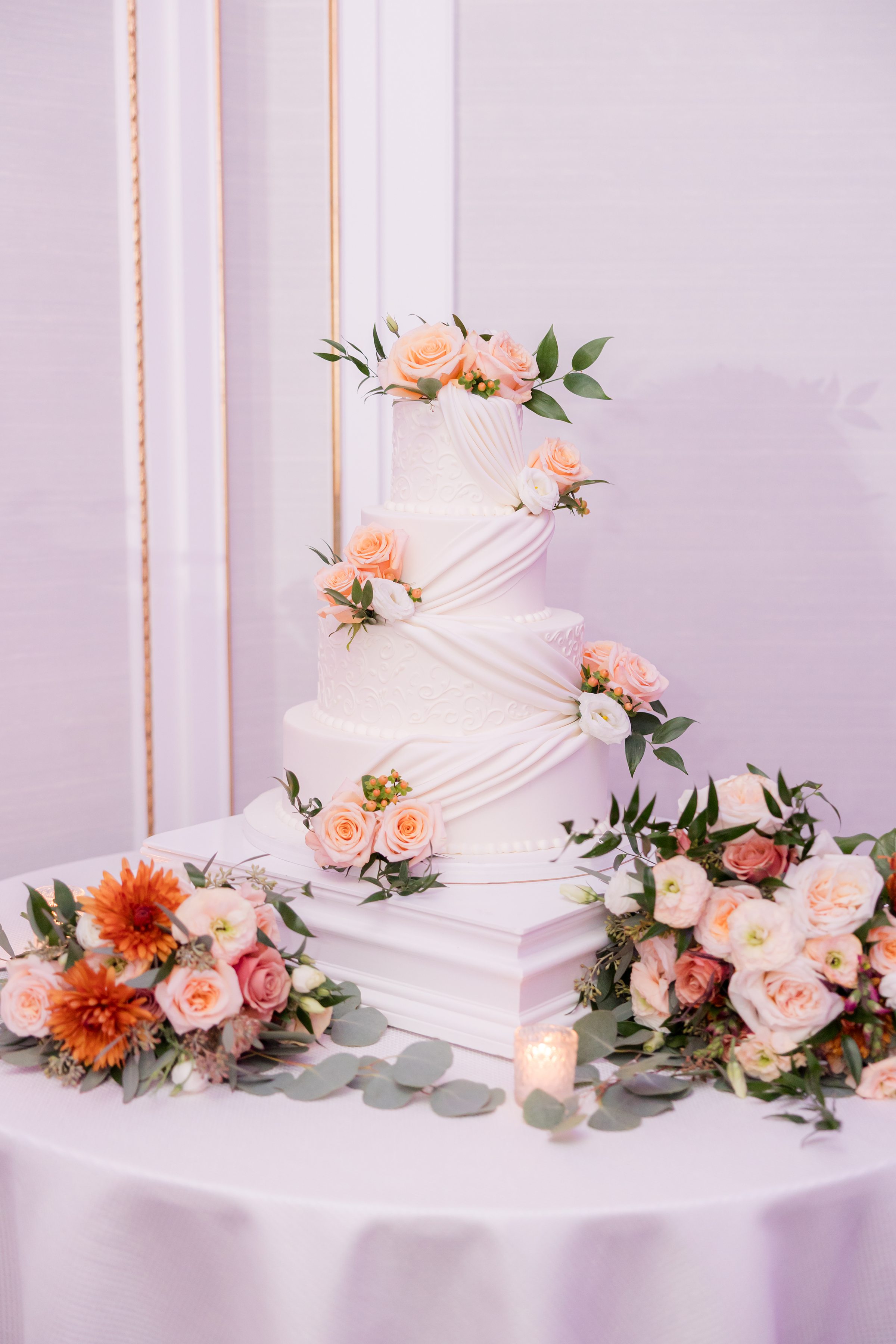 Elegant three-tier wedding cake decorated with peach roses and greenery.