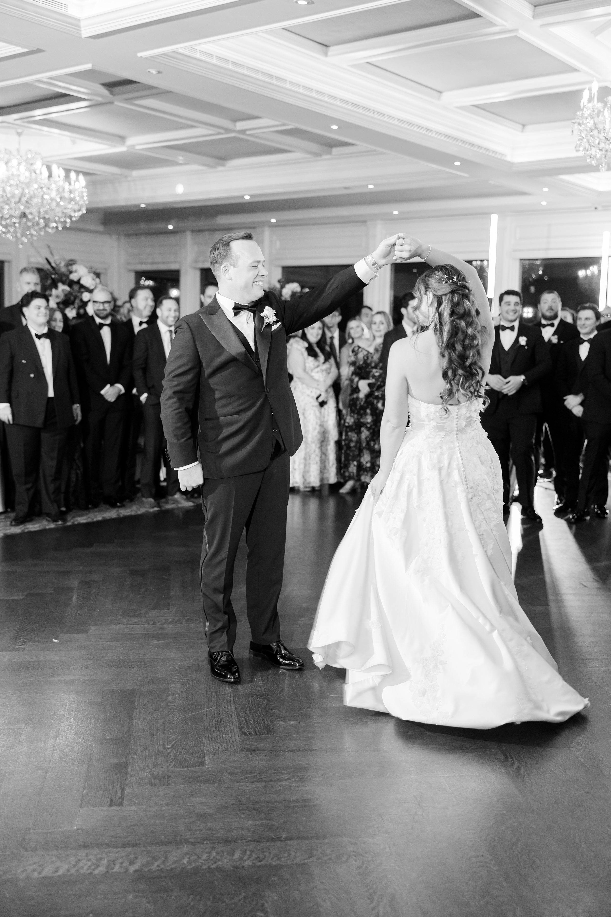 Groom twirls bride during their first dance while guests watch