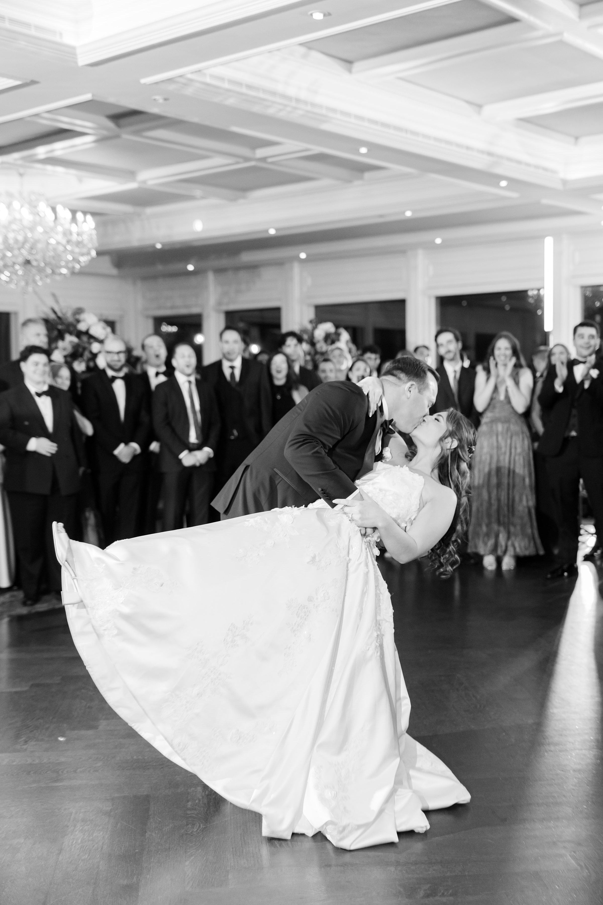 Groom dips bride for a kiss on the dance floor, surrounded by cheering guests