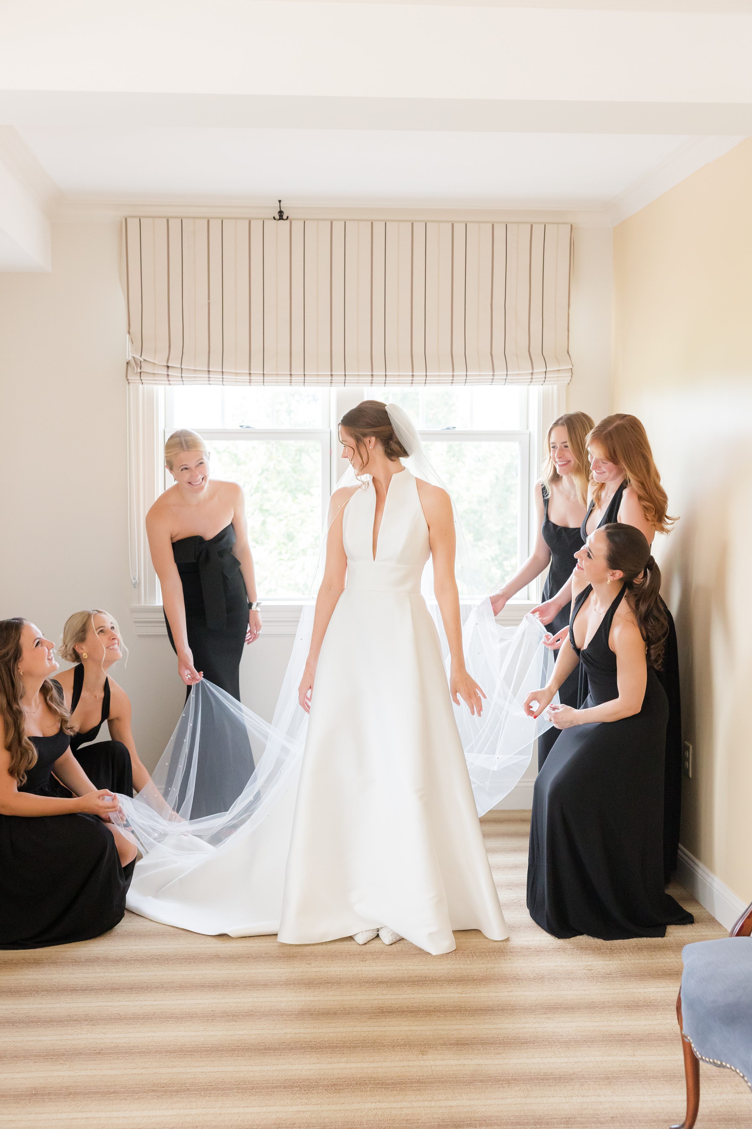 Bridesmaids gather around the bride, laughter and excitement filling the room as they help her prepare.