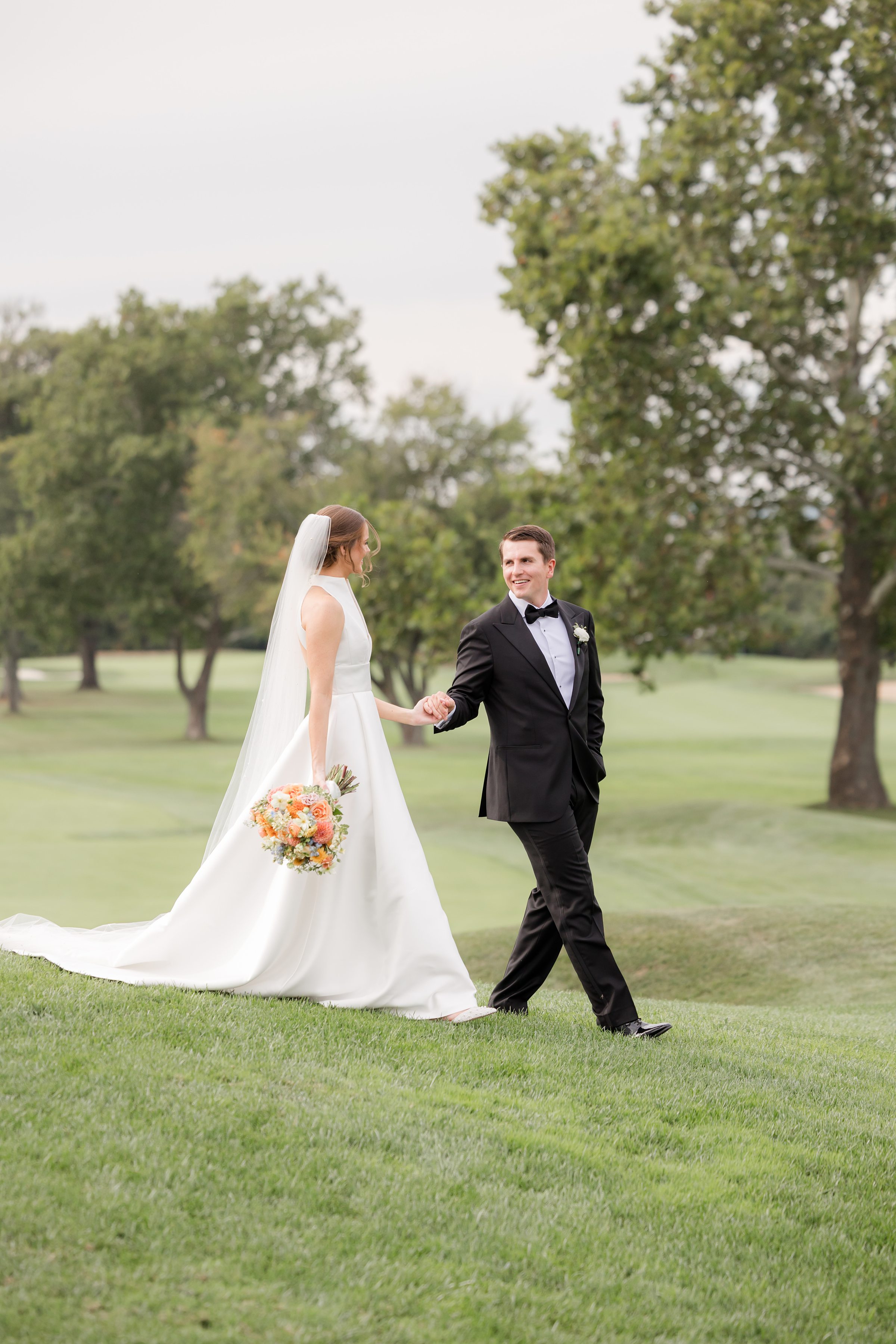 Bride and groom walk together through rolling green hills, sharing a quiet smile that speaks of love and forever.