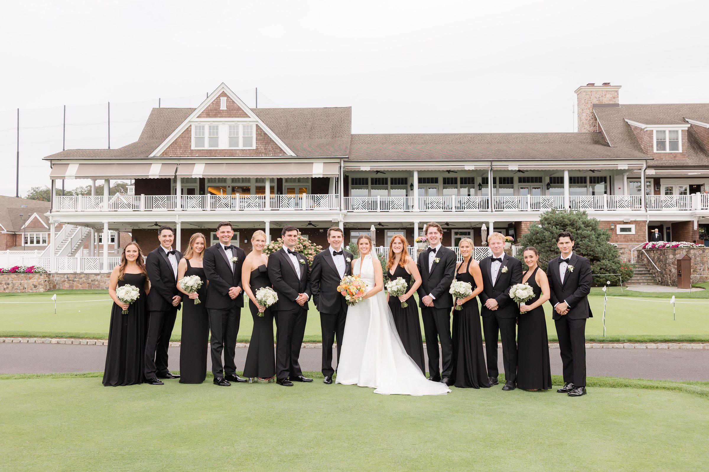 Bride and groom with bridesmaids and groomsmen posing in front of a country club venue on a golf course wedding day.