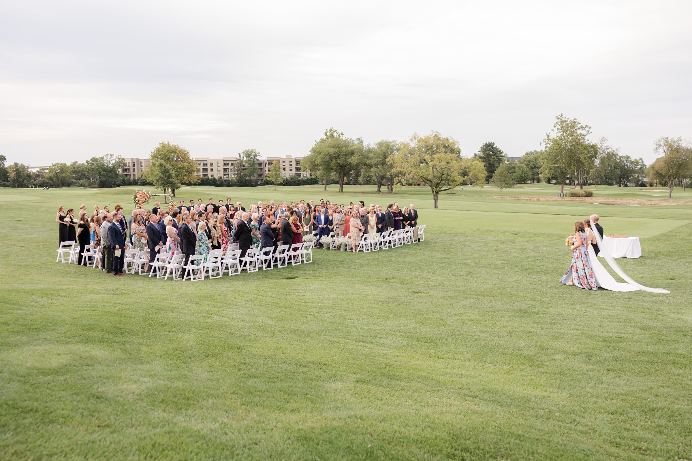 Bride walks gracefully down the aisle with her parents, her bouquet bright against her gown as loved ones look on