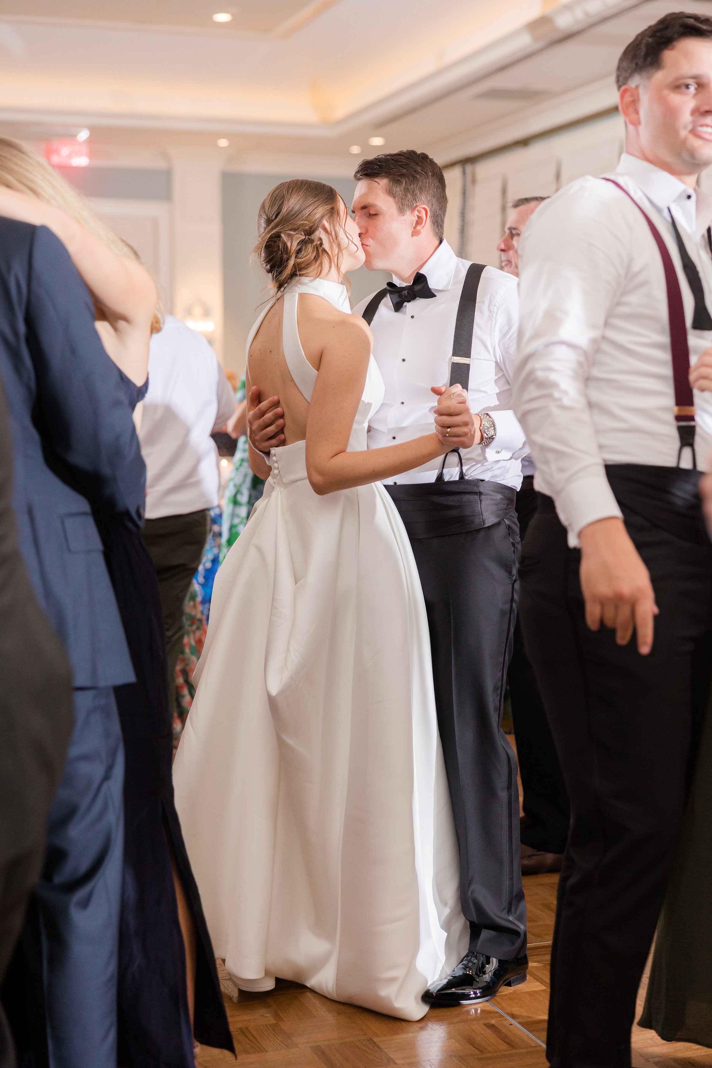 Bride and groom share a kiss on the dance floor, surrounded by guests during their wedding reception.