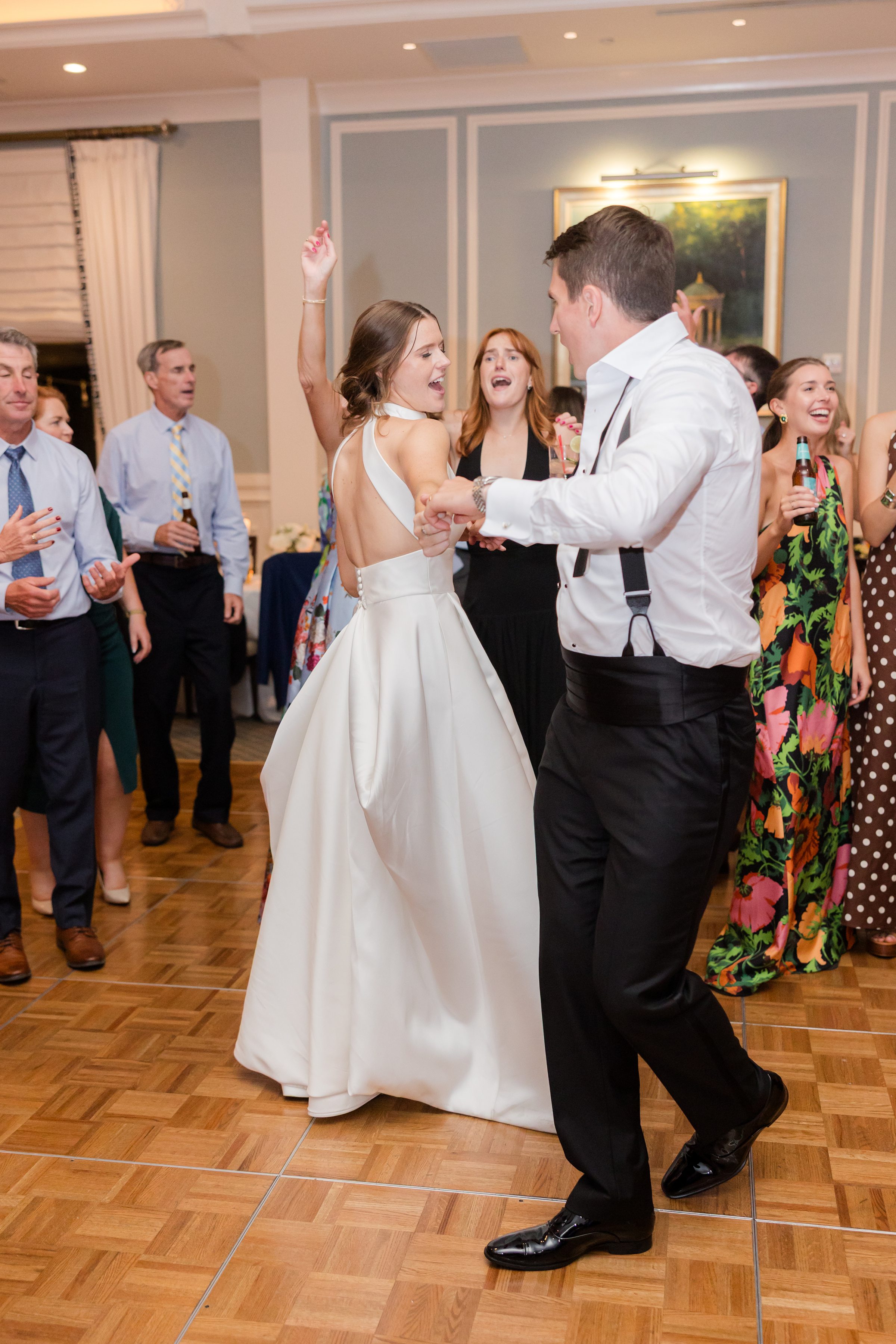 Bride and groom dance energetically on the reception dance floor, surrounded by cheering guests.
