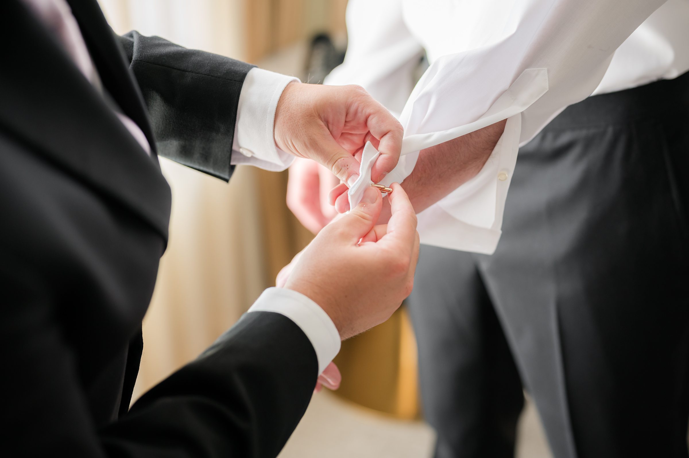 Groomsman carefully fastens the groom’s cufflink, a quiet, meaningful moment of friendship and support as they prepare for the wedding ceremony.