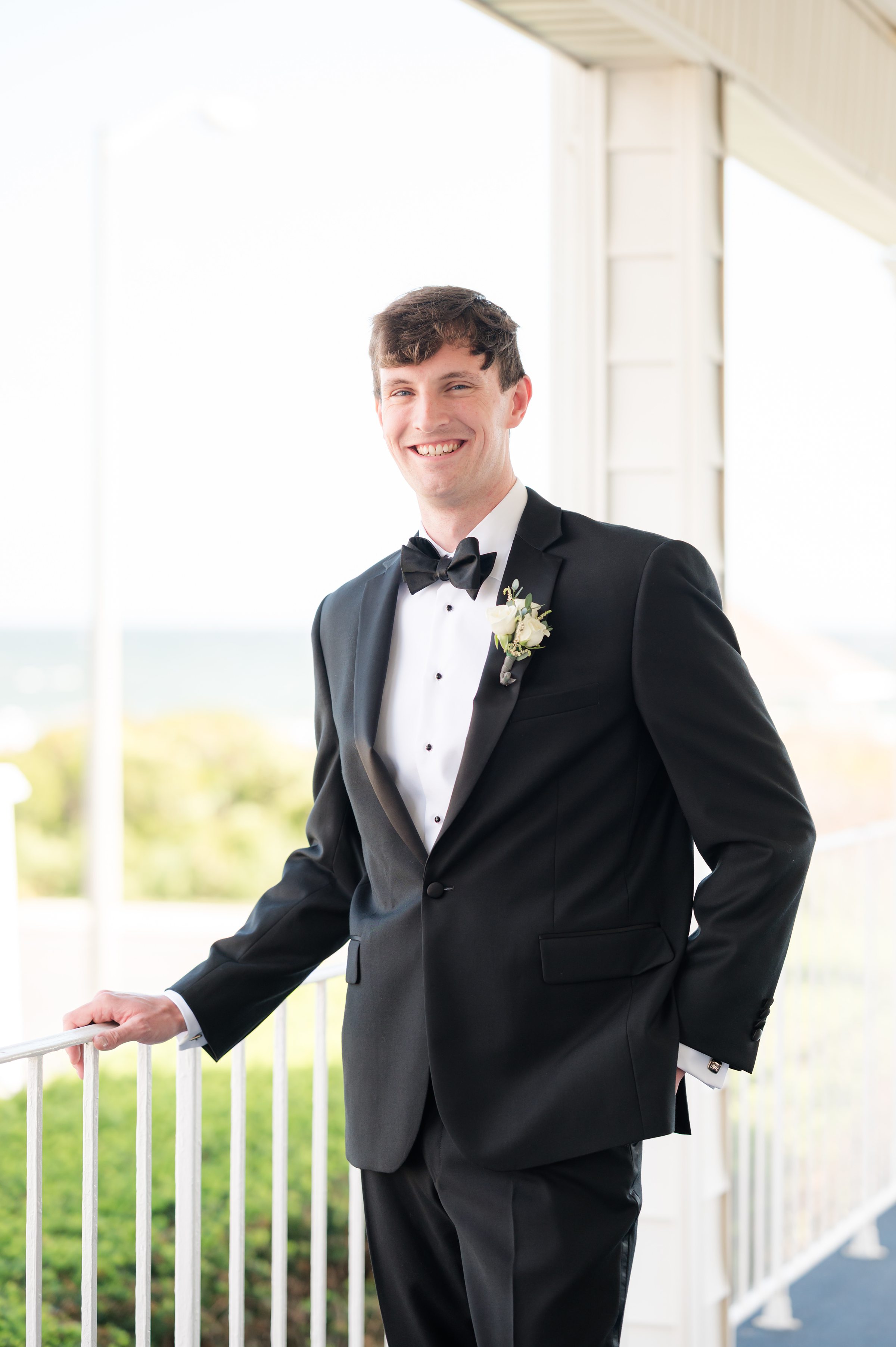 Groom leans casually with a warm smile, his eyes reflecting excitement and love for the day ahead.
