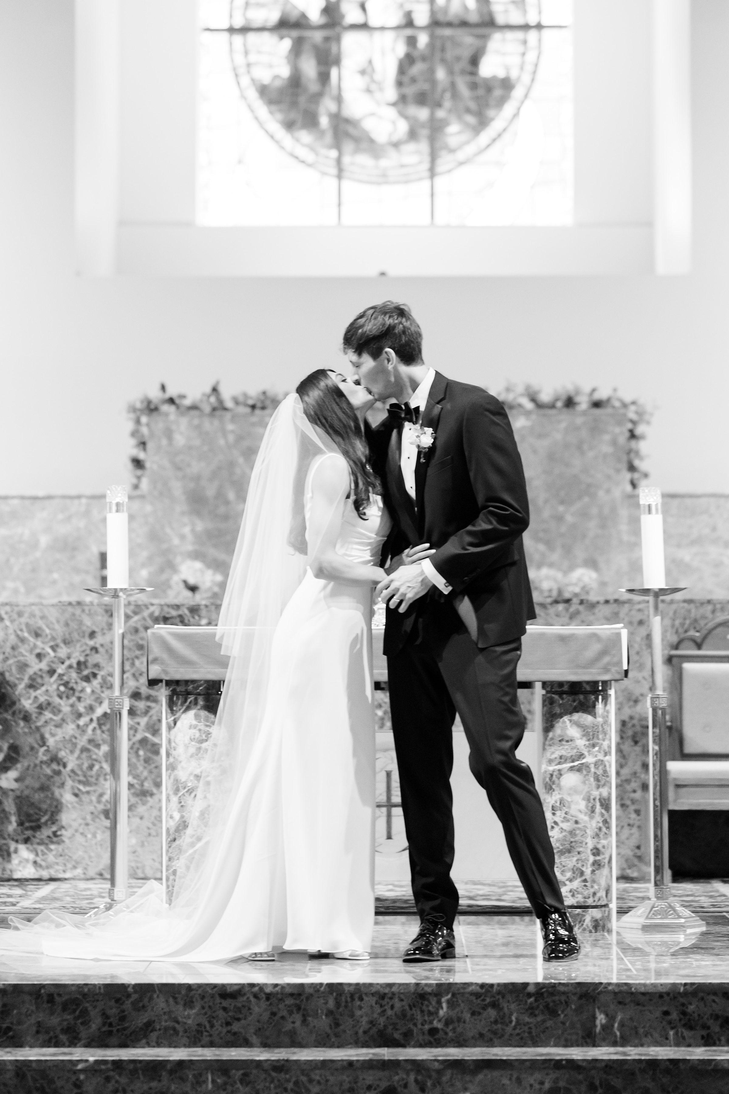 Beneath soft light and sacred stillness, the bride and groom share a tender kiss, beginning their forever.