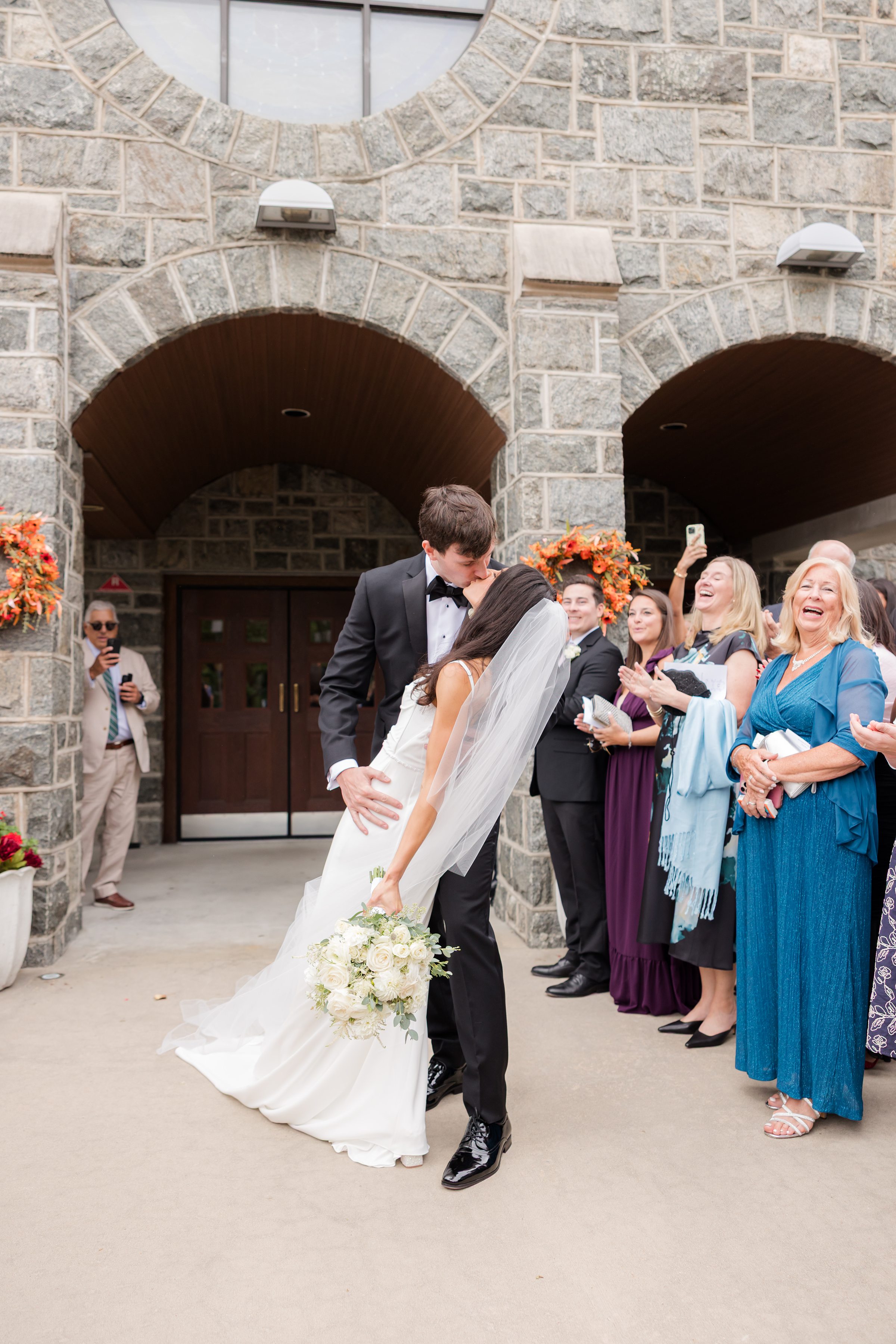 Celebrated by loved ones, the groom dips his bride into a kiss filled with passion and celebration.