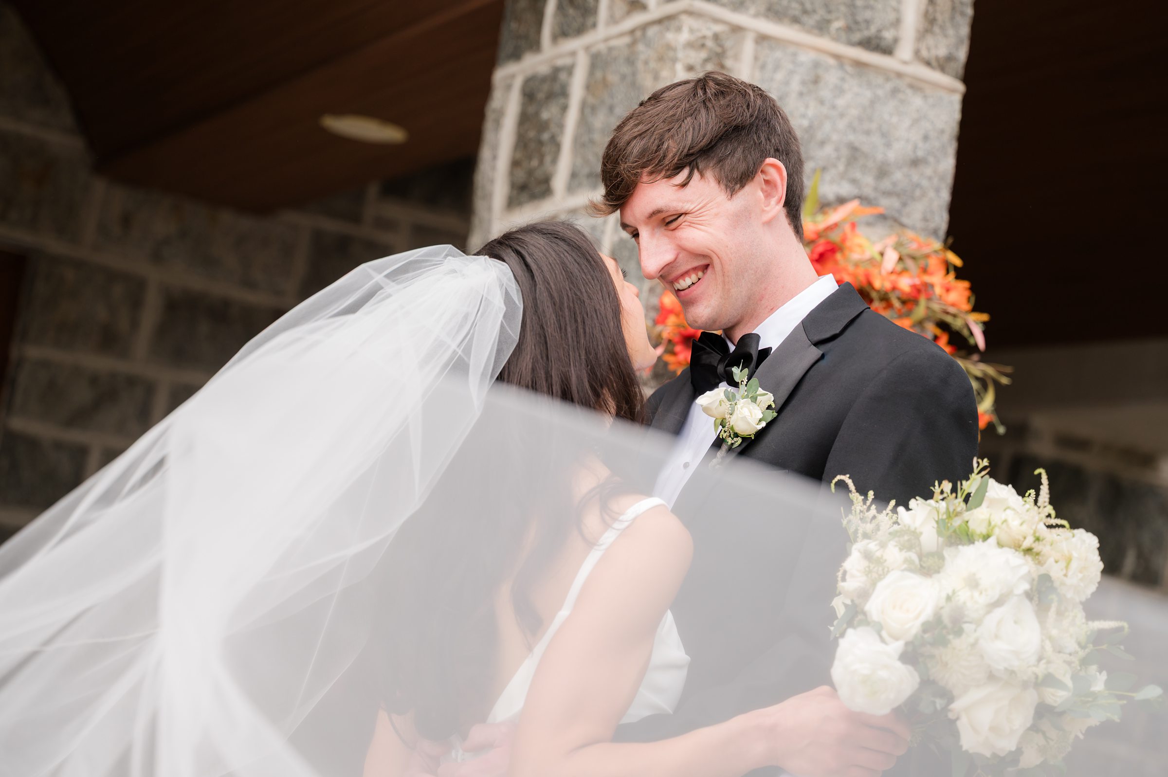 Wrapped in soft light and flowing veil, the bride and groom share a tender, joyful moment just for each other.