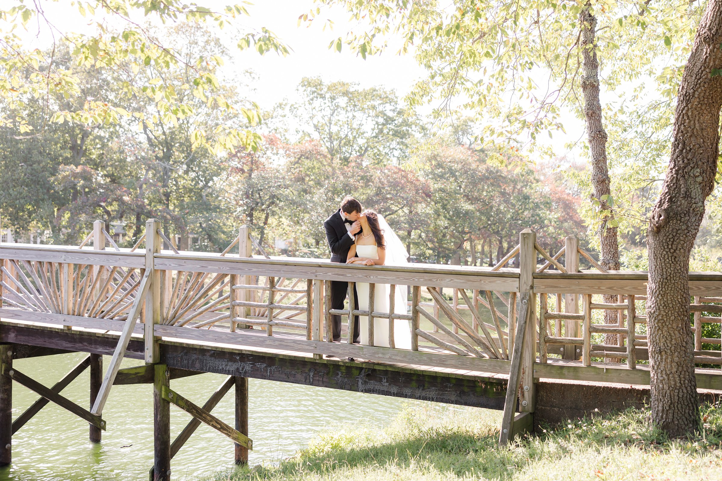 Sunlit bridge, the bride and groom share a tender kiss, surrounded by soft light and the quiet beauty of nature.