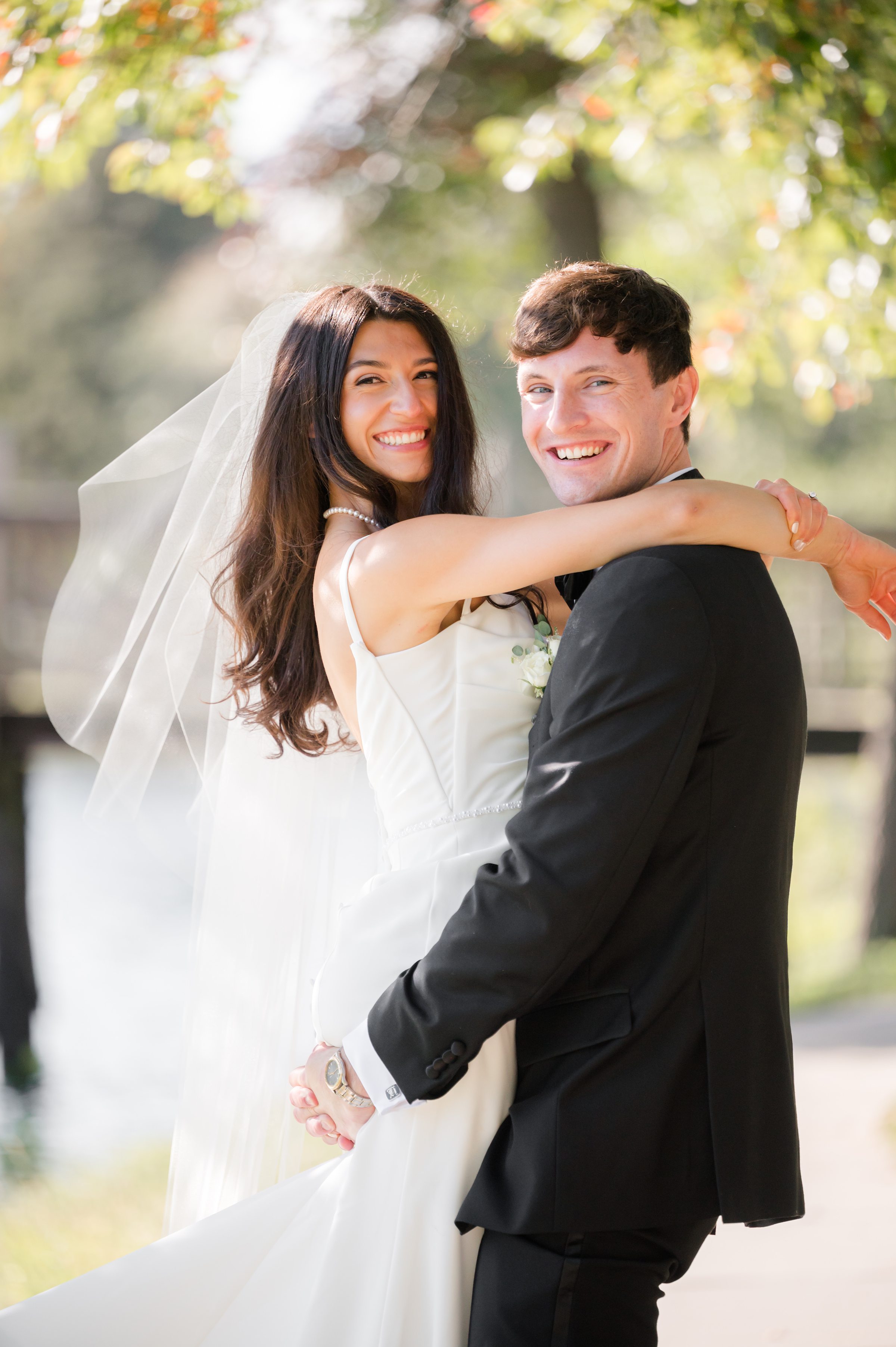 Bride wraps her arms around her groom as they smile back together, glowing with happiness in soft, golden light.