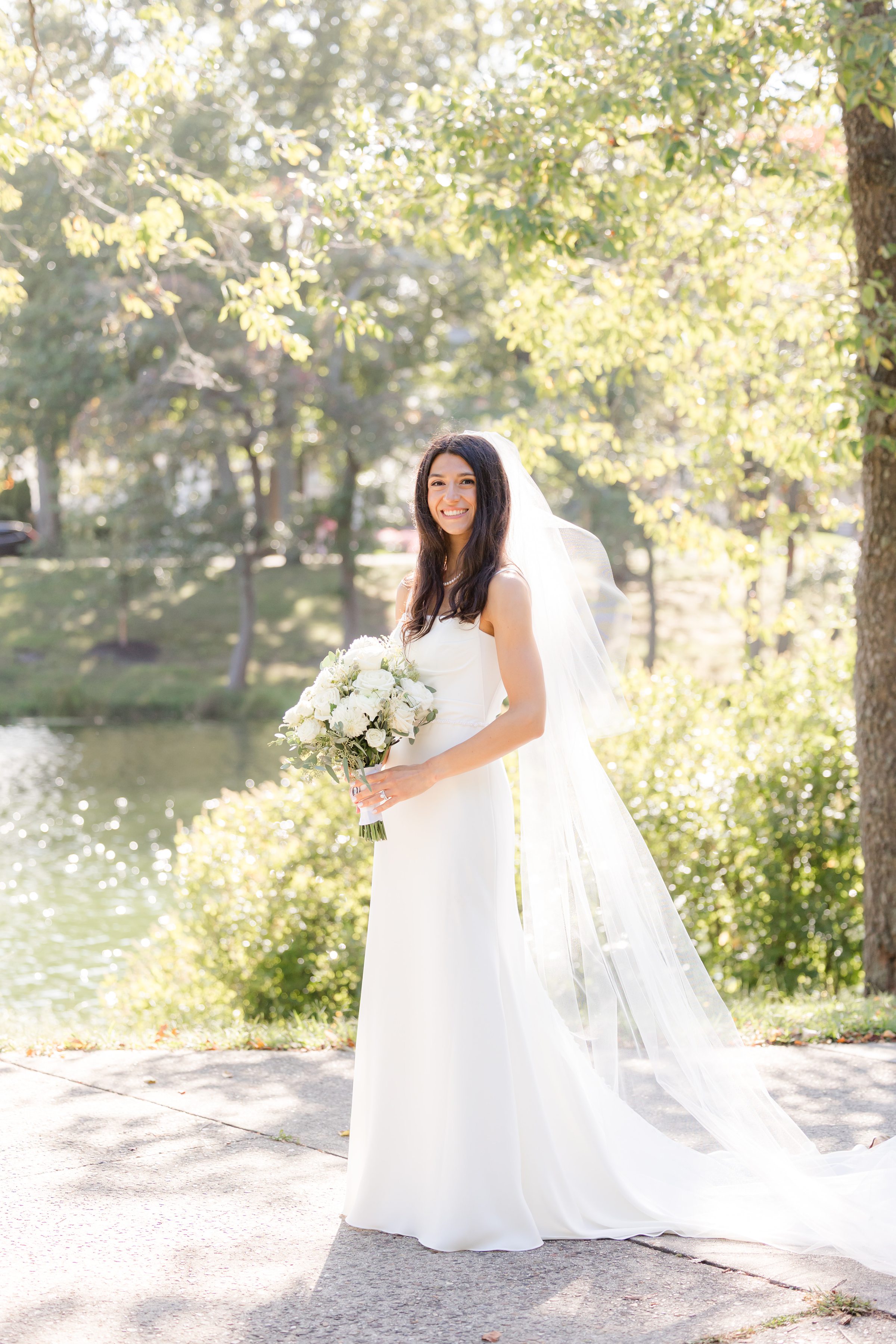 Bride stands by the water, glowing with elegance and the promise of a new beginning.