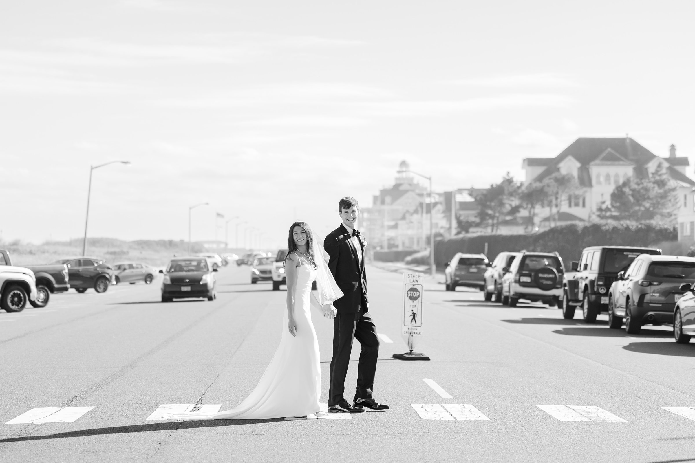 Bride and groom stand together in the middle of a quiet coastal street, sharing a bold, cinematic moment together as the world moves softly around them.