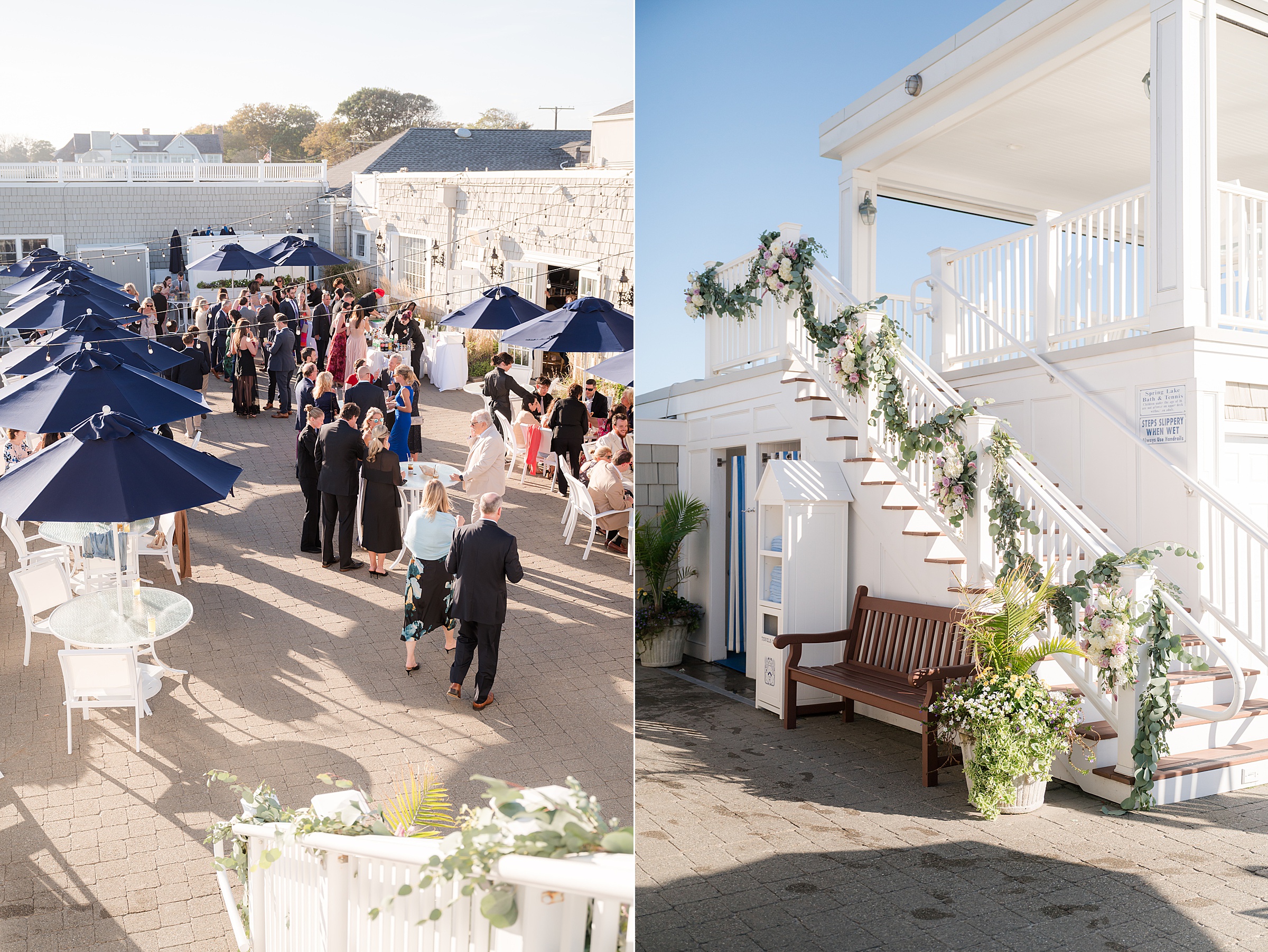 Guests gather and mingle under navy umbrellas in a sunlit courtyard, while a nearby white staircase draped in greenery and soft florals adds an elegant, romantic touch to the wedding setting.