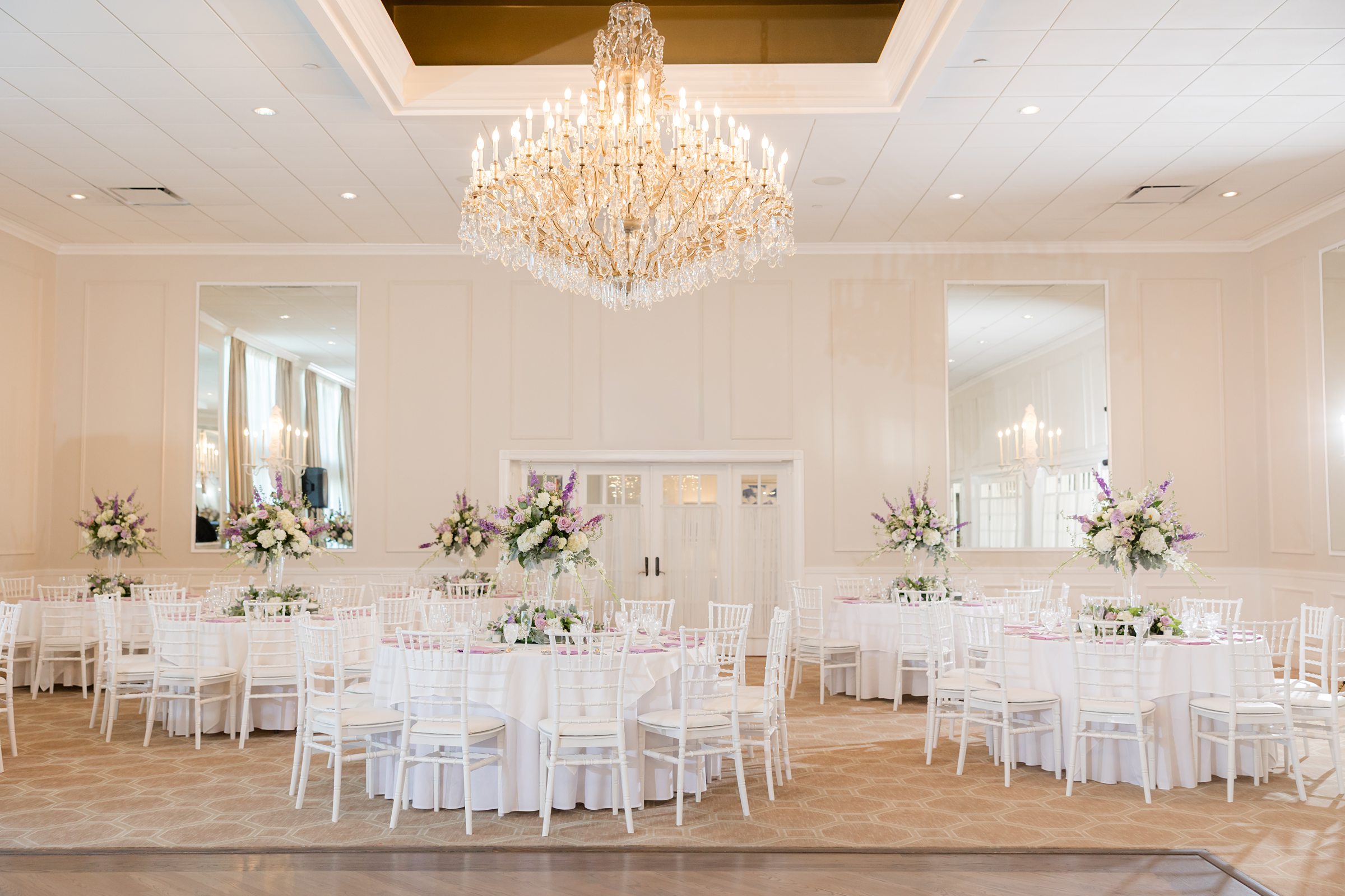 Wedding reception hall sparkles beneath a grand chandelier, with carefully arranged tables and florals creating a dreamy, romantic atmosphere.