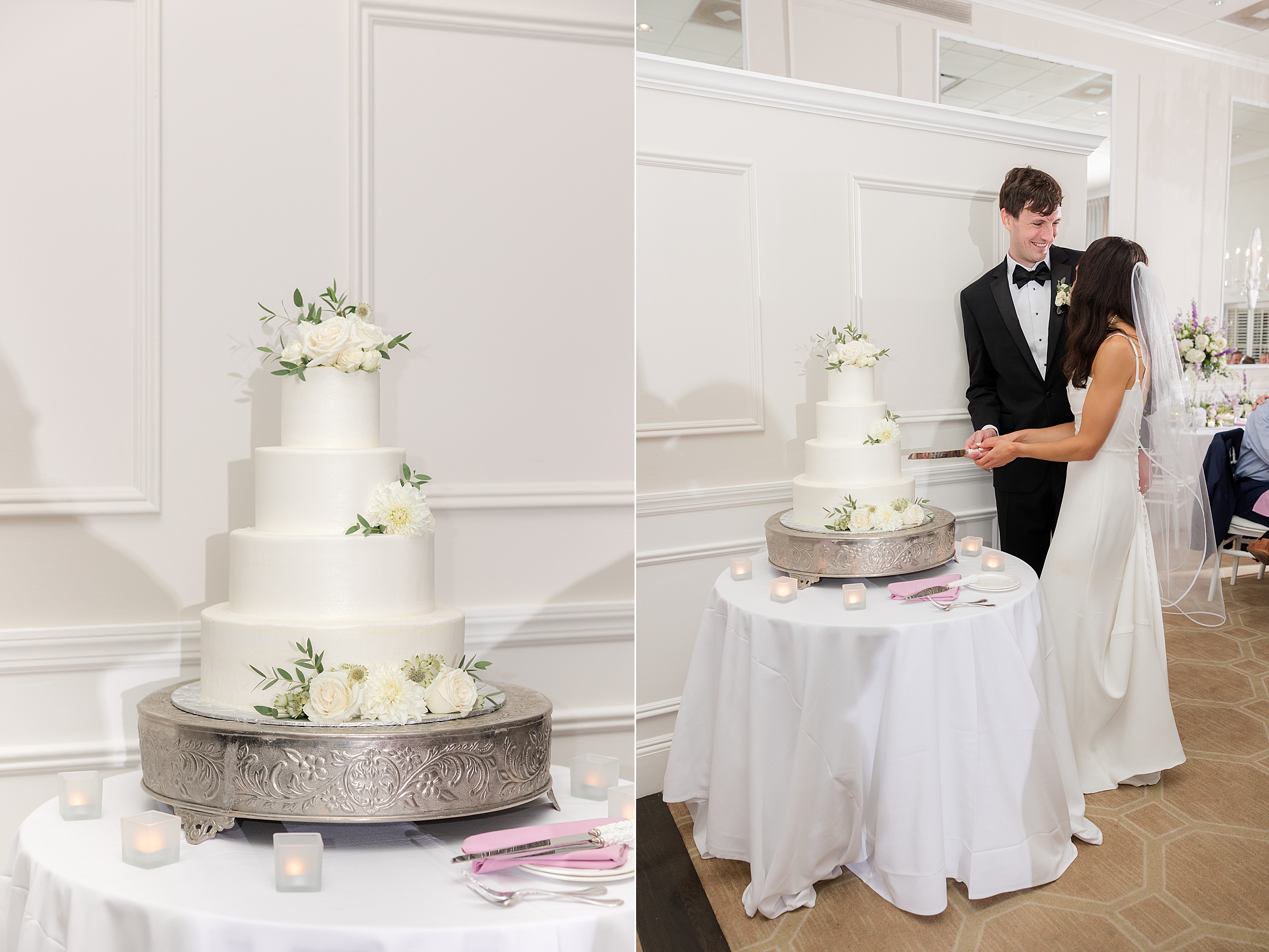 Elegant white tiered wedding cake adorned with soft florals beside the bride and groom smiling as they prepare to cut it together.