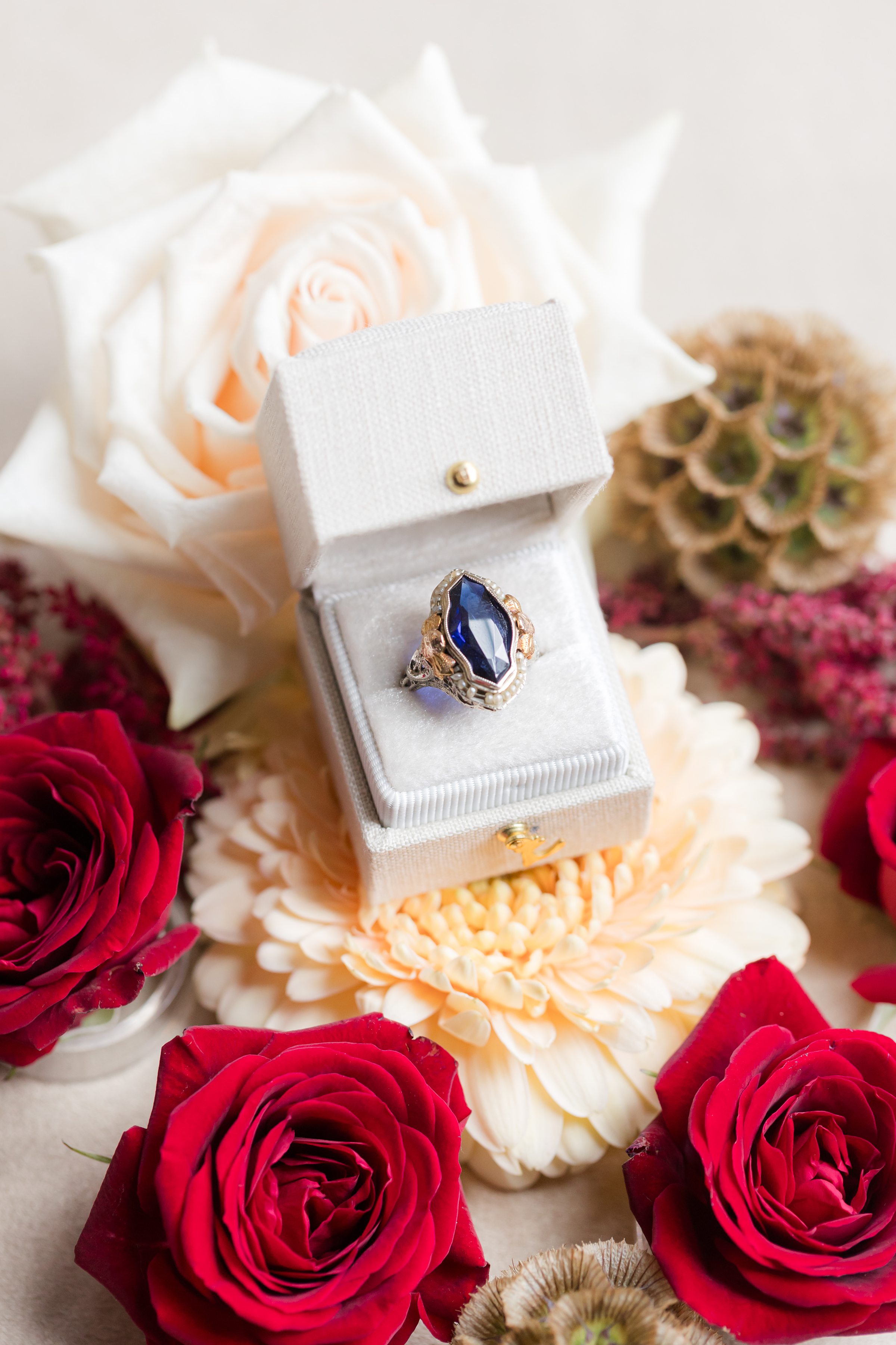 Blue gemstone ring in an open velvet box surrounded by red and white flowers.