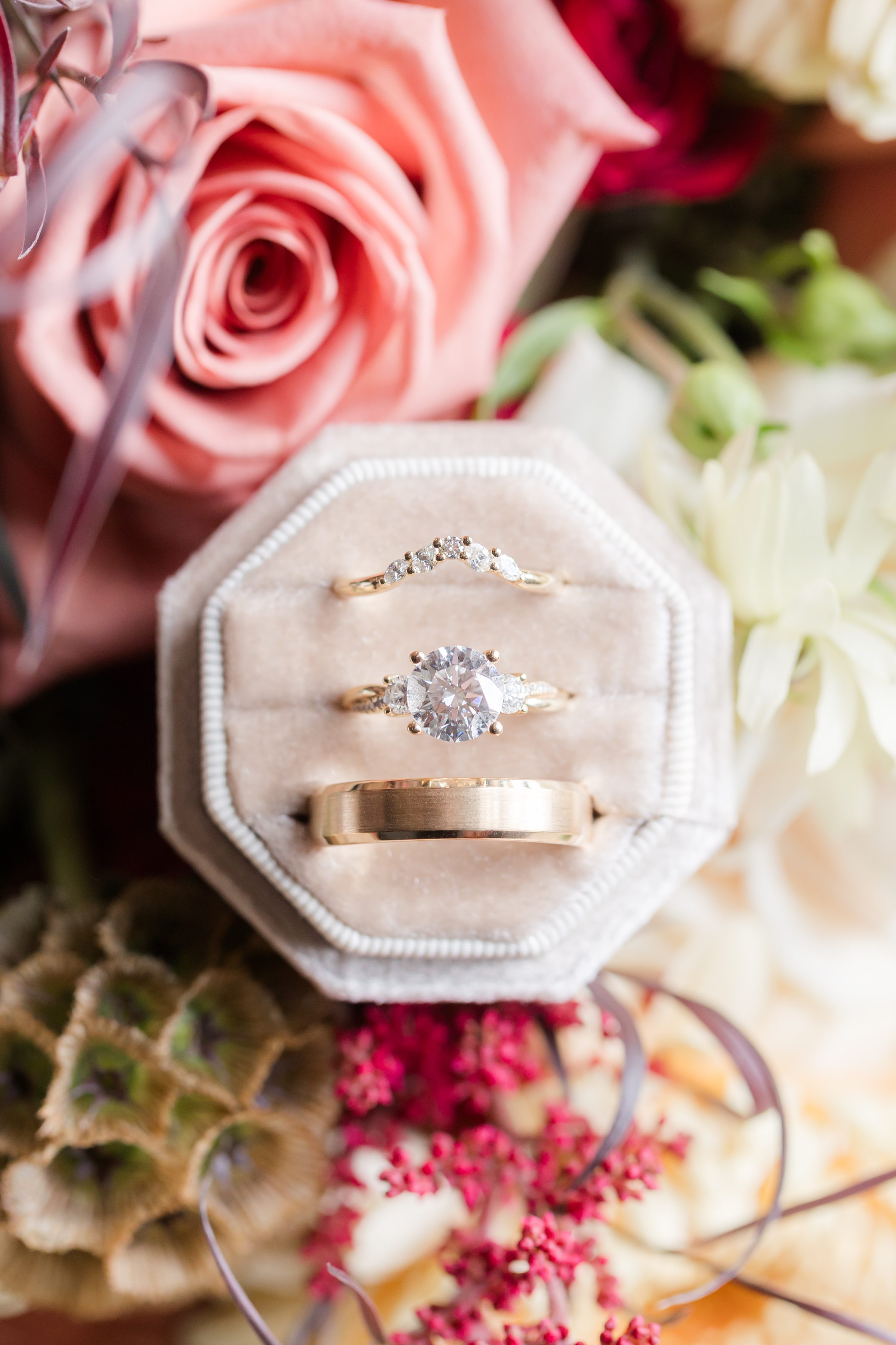 Three gold rings in a velvet box surrounded by pink and white flowers.