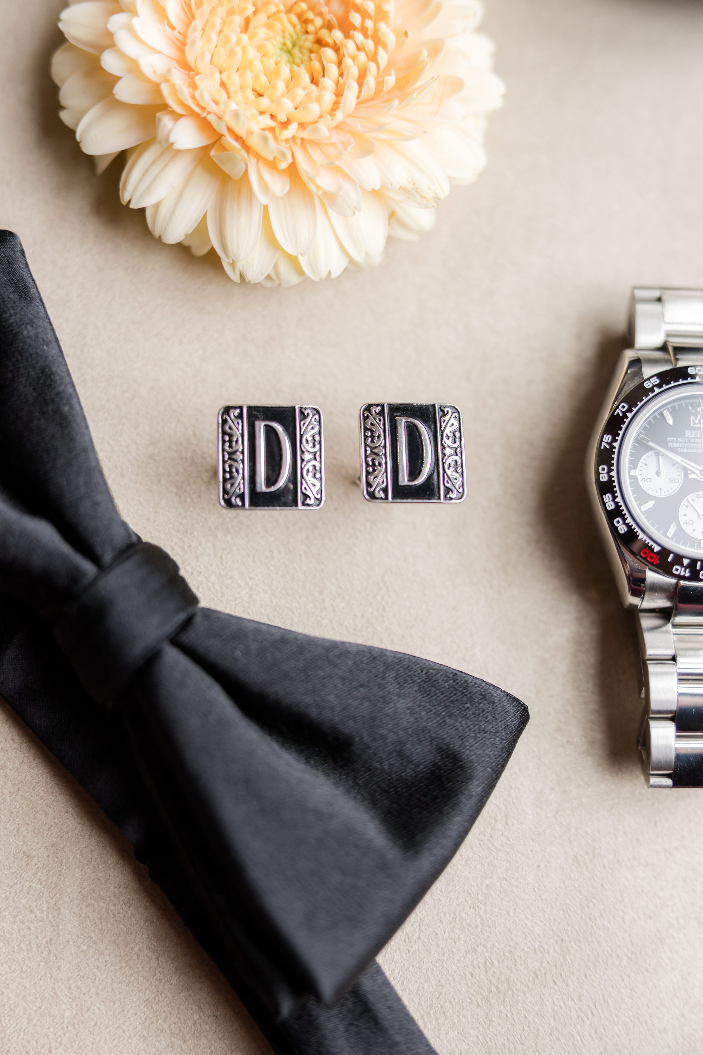 Groom’s cufflinks, black bow tie, watch, and a soft cream flower.