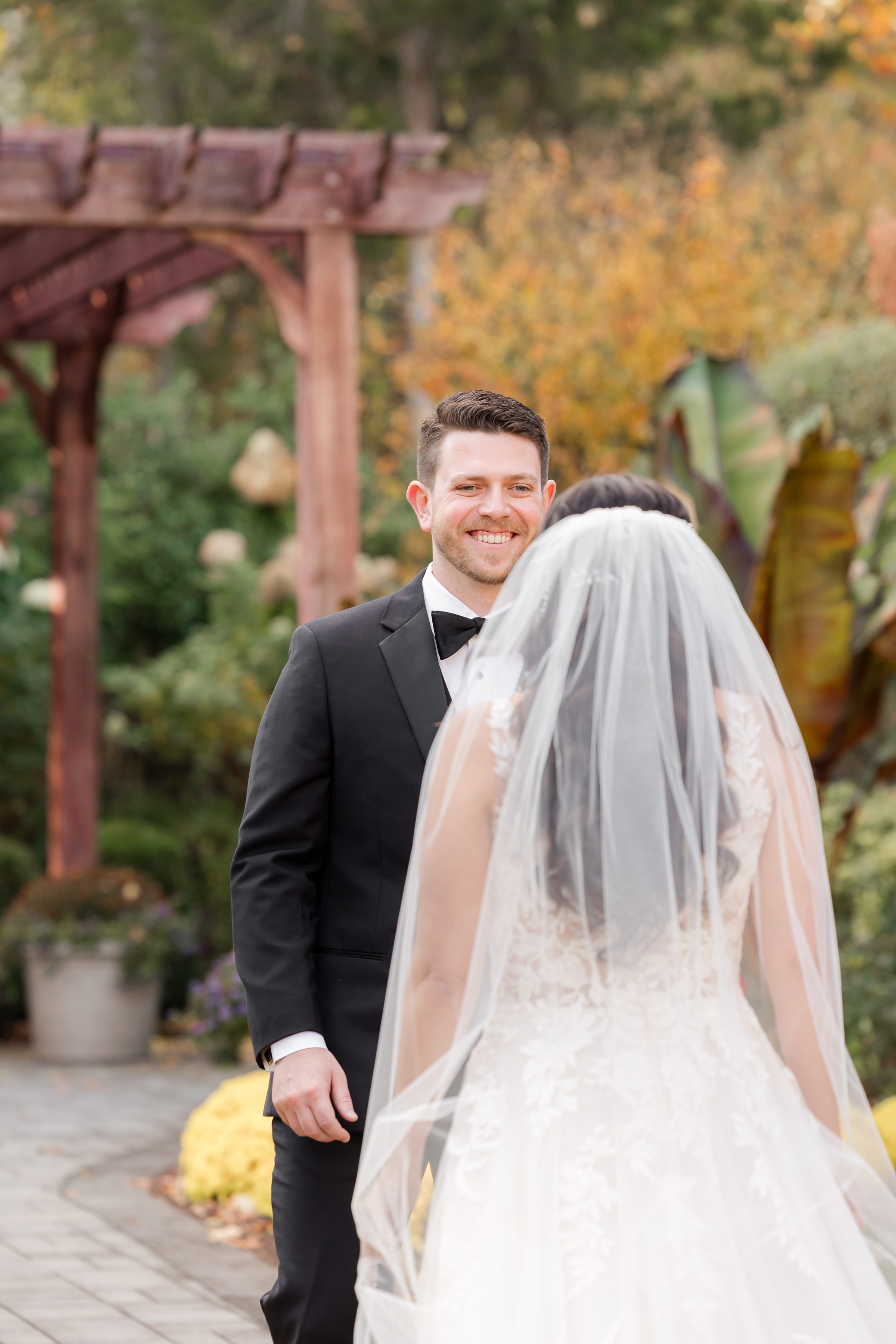 Groom smiling as he sees his bride during their first look in a garden setting.